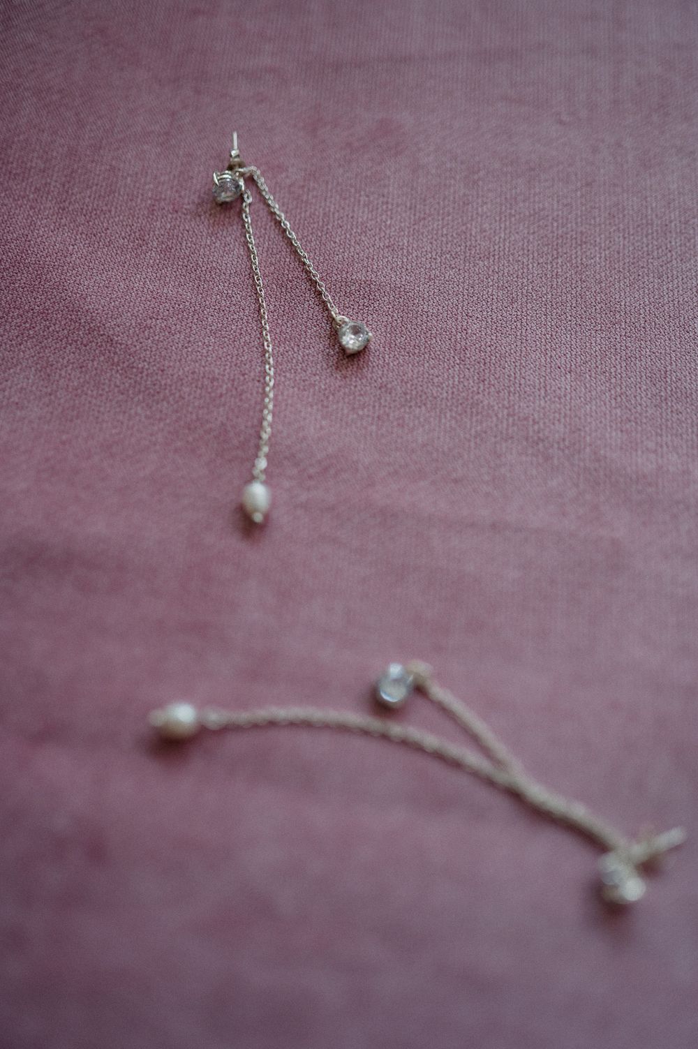 Delicate silver chain drop earrings with pearl and crystal accents on a dusty rose fabric background.