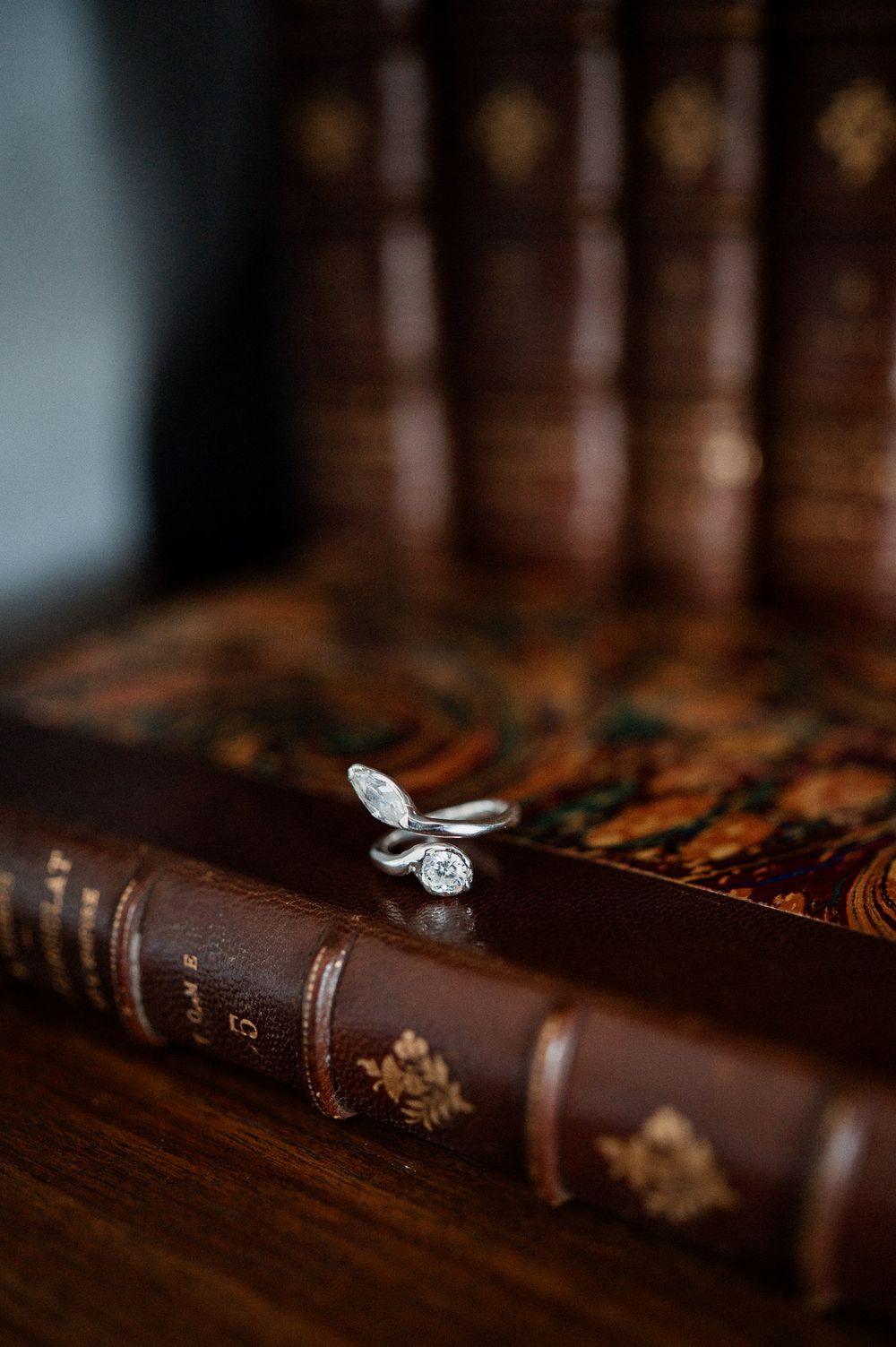 Elegant diamond engagement ring resting on antique leather-bound books with gold embossed spines in a library setting.