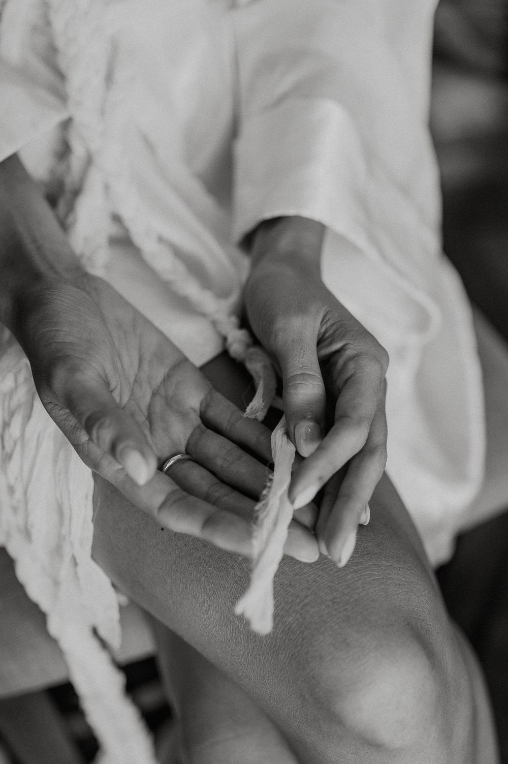 Close-up black and white photo of hands holding a twisted rope detail on a white wedding dress.