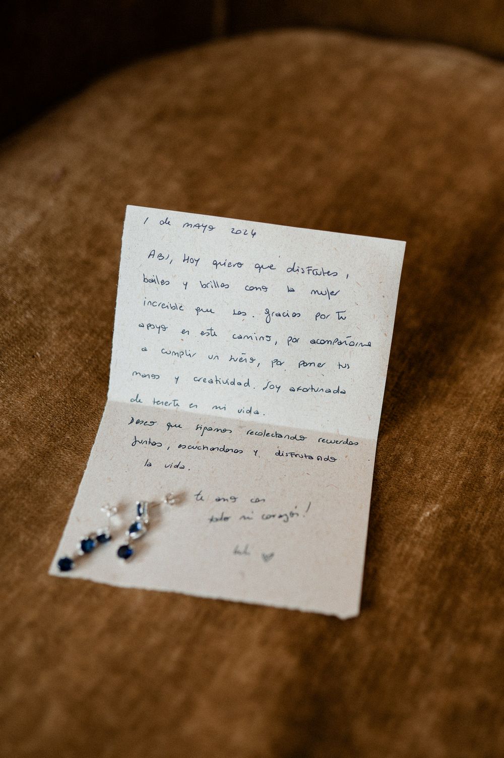 Handwritten love letter in Spanish dated May 1, 2024, with blue crystal earrings resting on beige fabric.