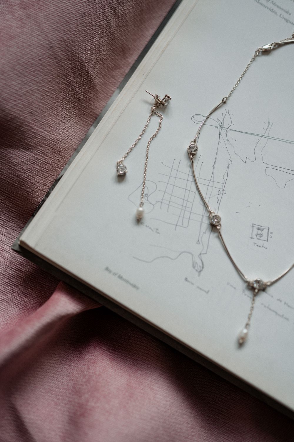 Delicate silver pearl drop earrings and matching necklace displayed on an open book with pink satin fabric.