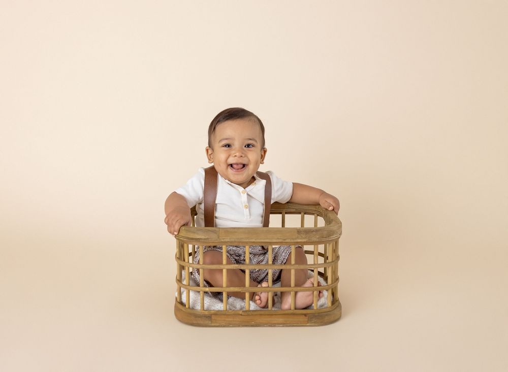 Smiling baby boy sitting in a rustic wooden basket crate during a professional studio portrait session.