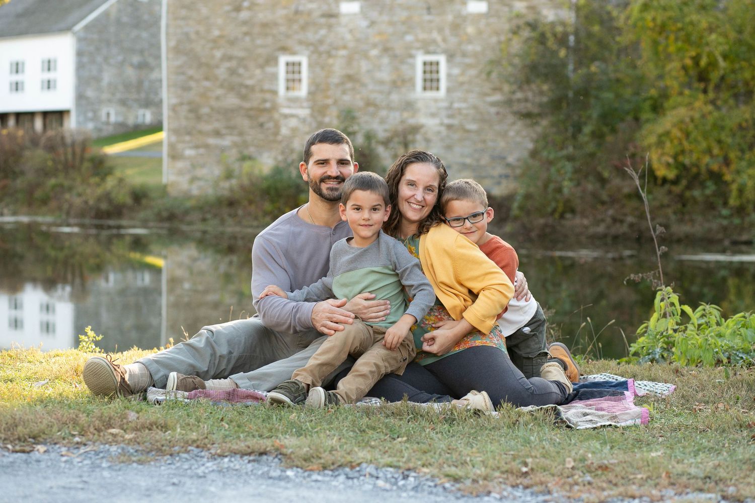 Family of four posing by a peaceful river surrounded by autumn foliage during a fall outdoor photo session.