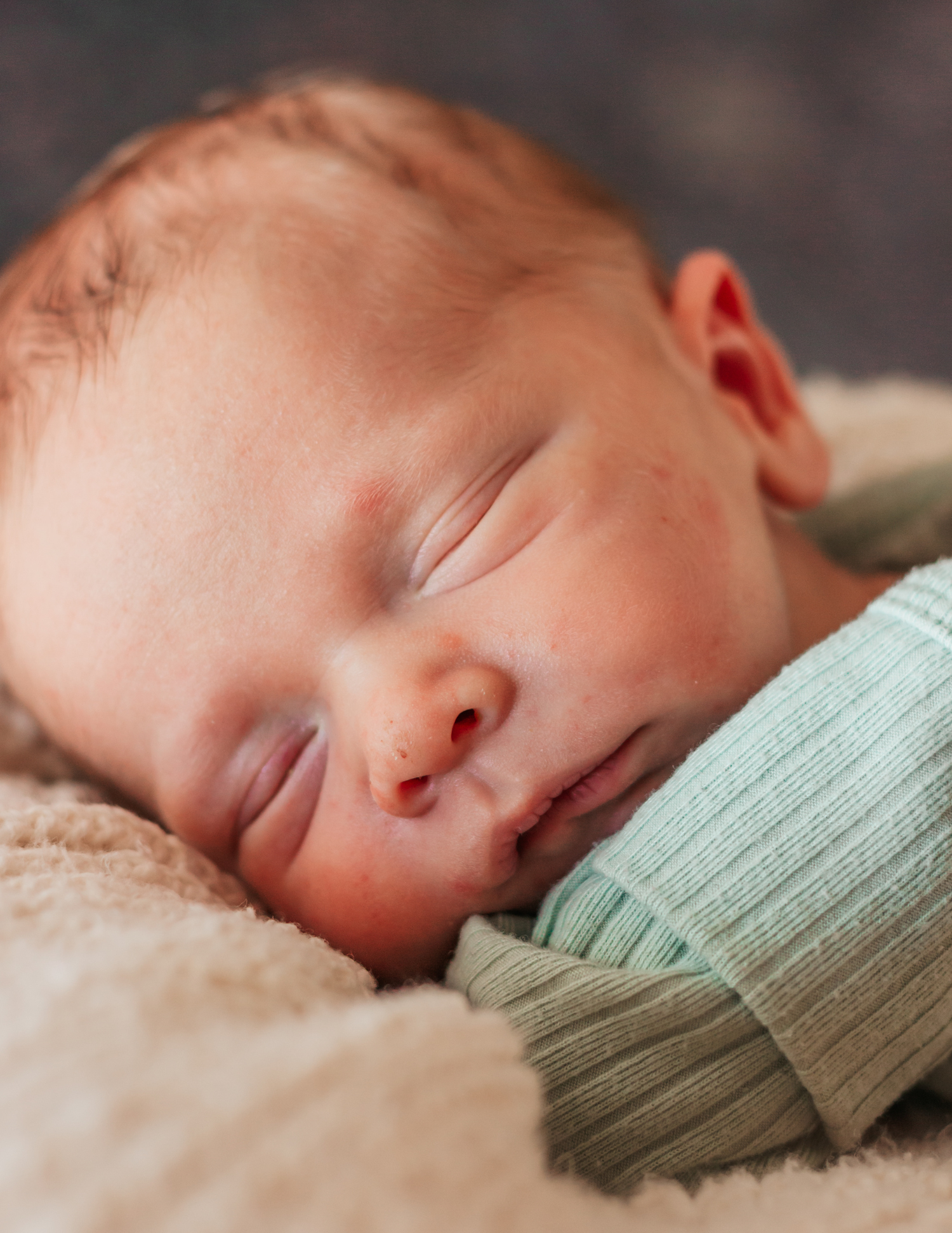 Peaceful newborn baby sleeping soundly on a soft beige blanket, wearing a light green ribbed onesie.
