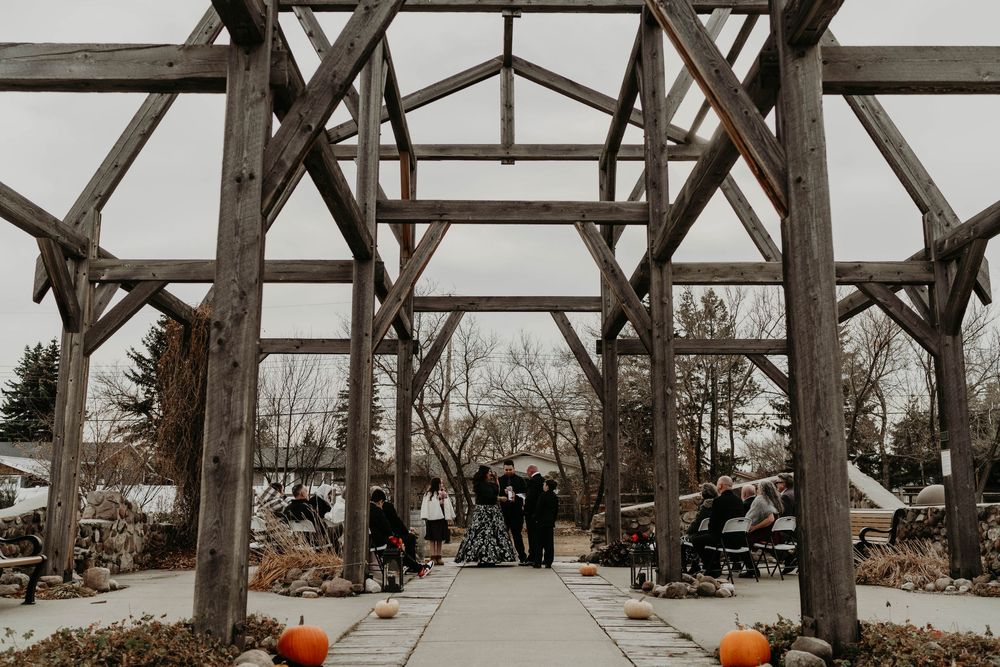 Wedding ceremony under rustic wooden pergola with pumpkins lining the aisle on a cloudy autumn day.