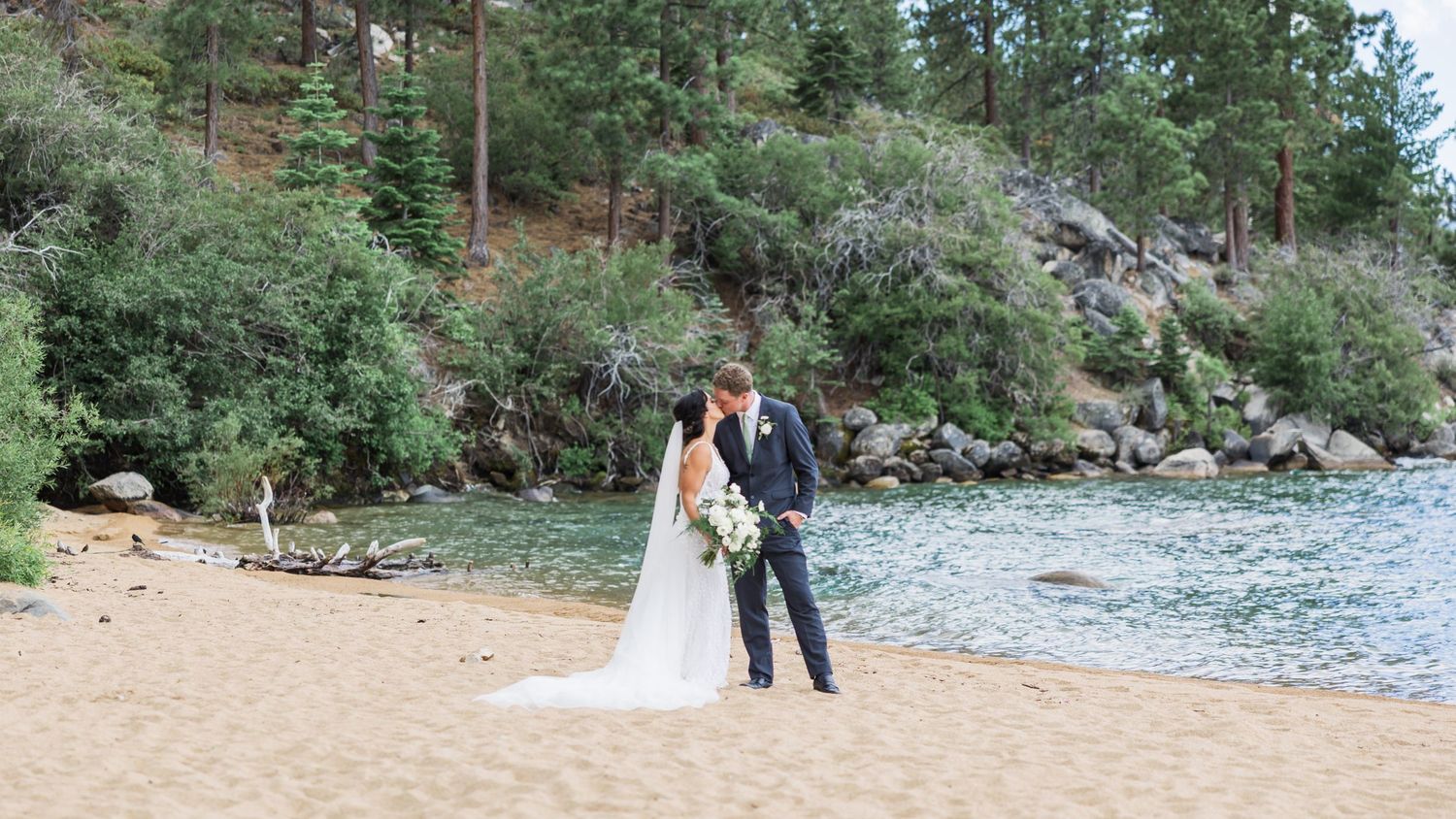 Couple embracing on a wooden bridge surrounded by lush greenery and blooming pink flowers in a romantic garden setting.