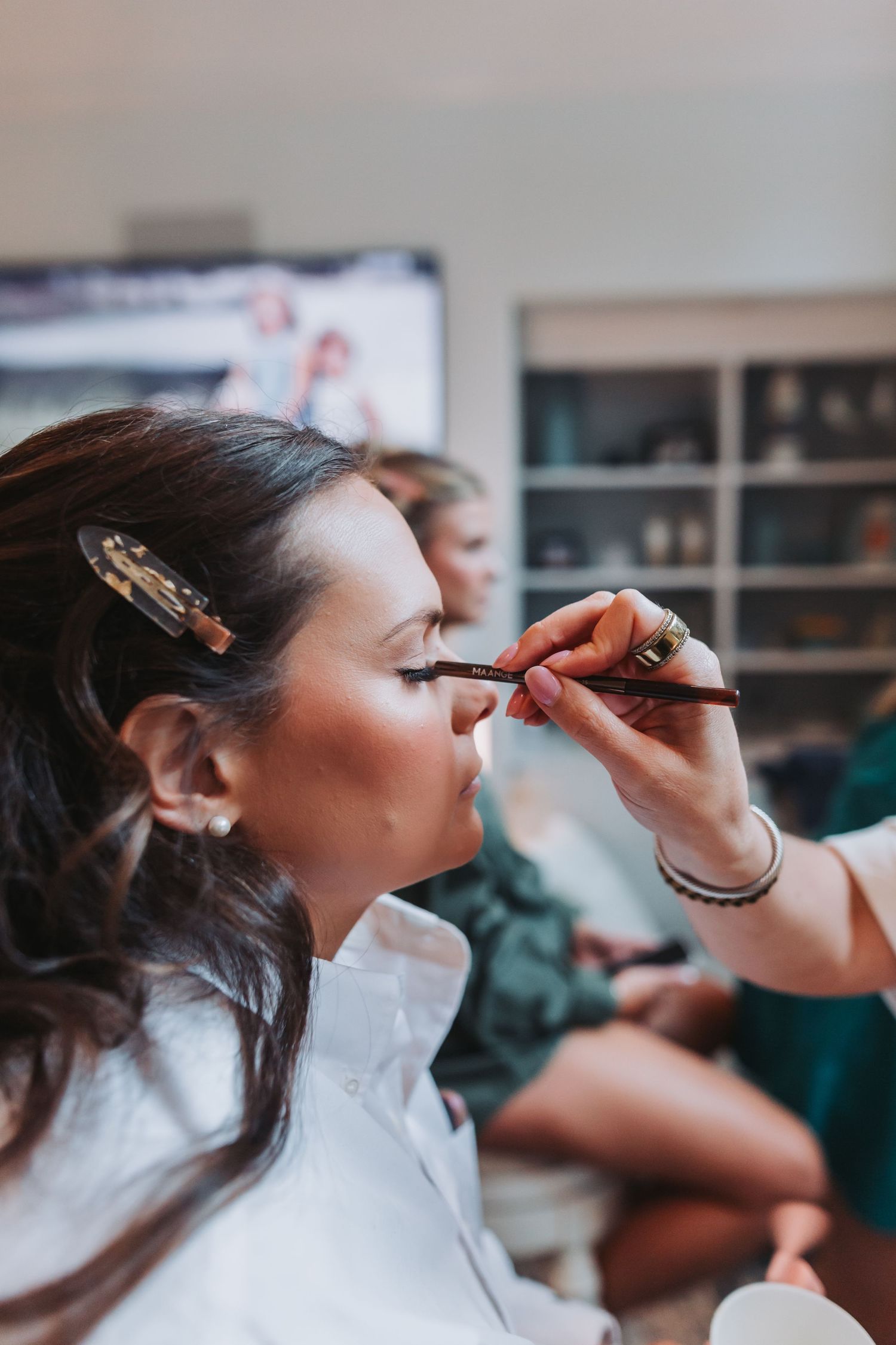 Makeup artist applying eyeliner to a brunette bride during wedding preparations.