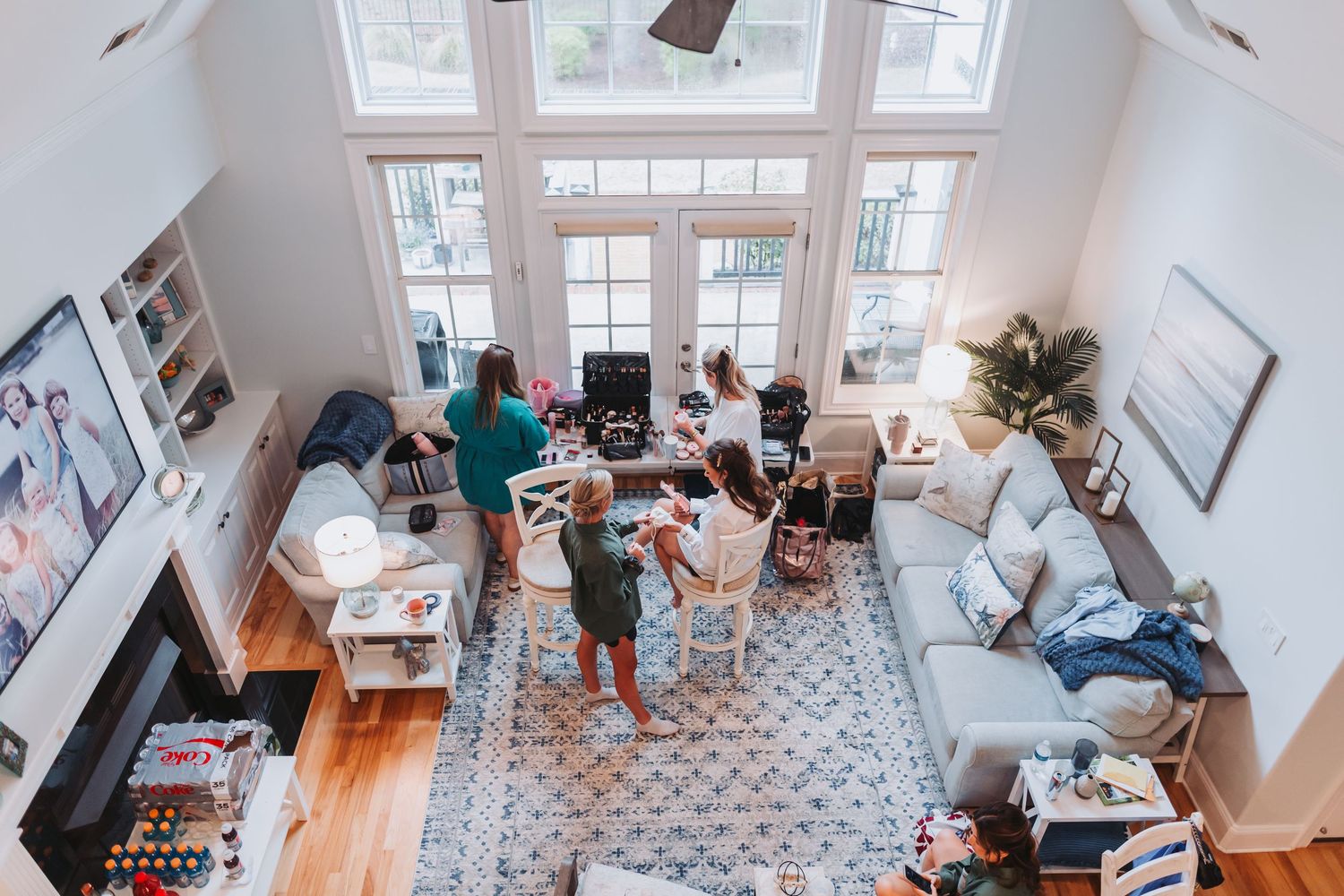 Aerial view of bridal party getting ready in bright open-concept living room with high ceilings.