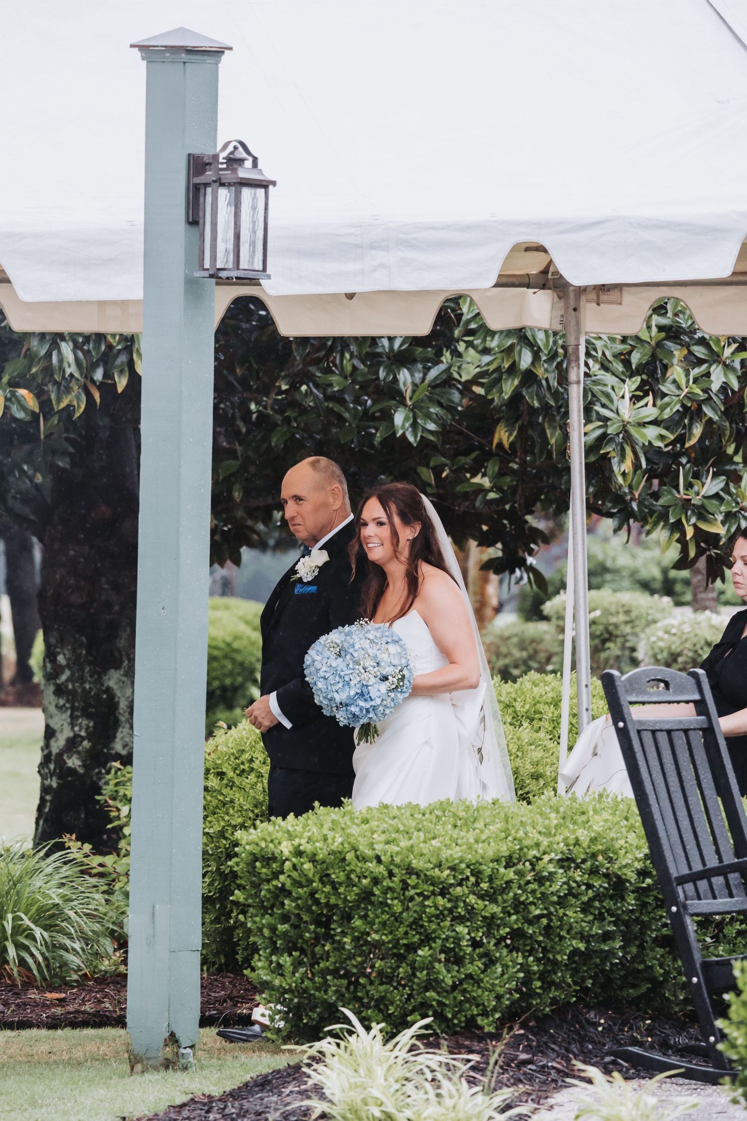 Bride with blue hydrangea bouquet walking down aisle with escort at outdoor wedding.