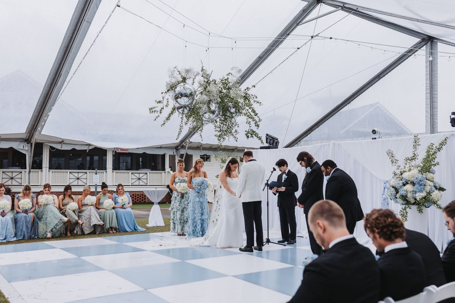 Bride and groom exchange vows at outdoor tented wedding ceremony on black and white checkered dance floor.