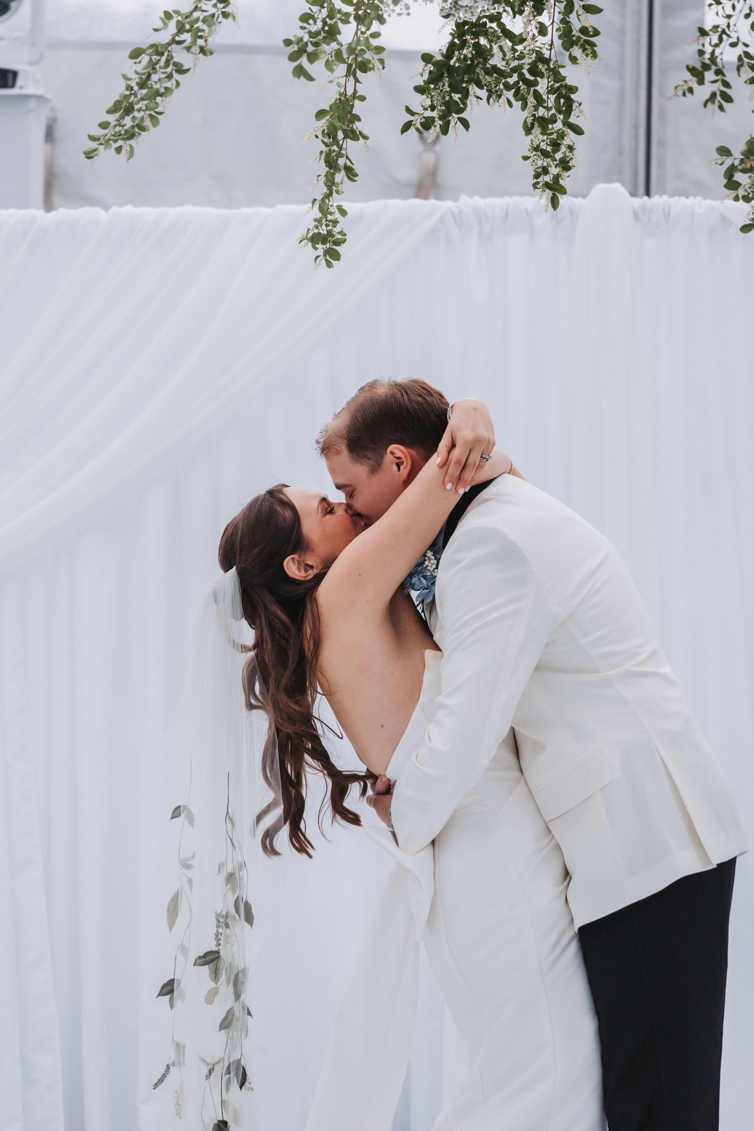 Bride and groom share their first kiss at the altar, surrounded by white draping and greenery.