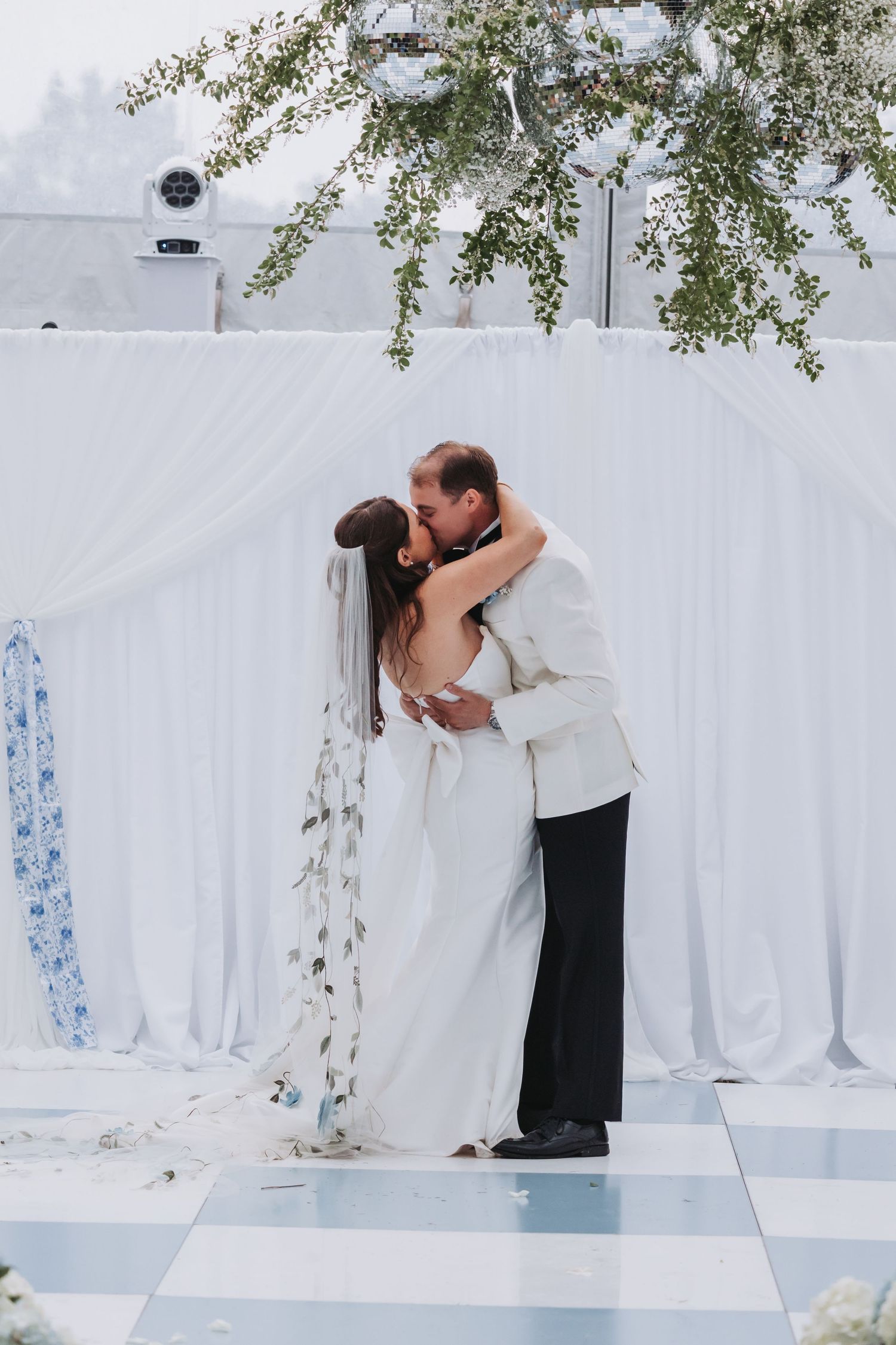 Bride and groom share their first kiss at a white draped outdoor wedding ceremony altar.
