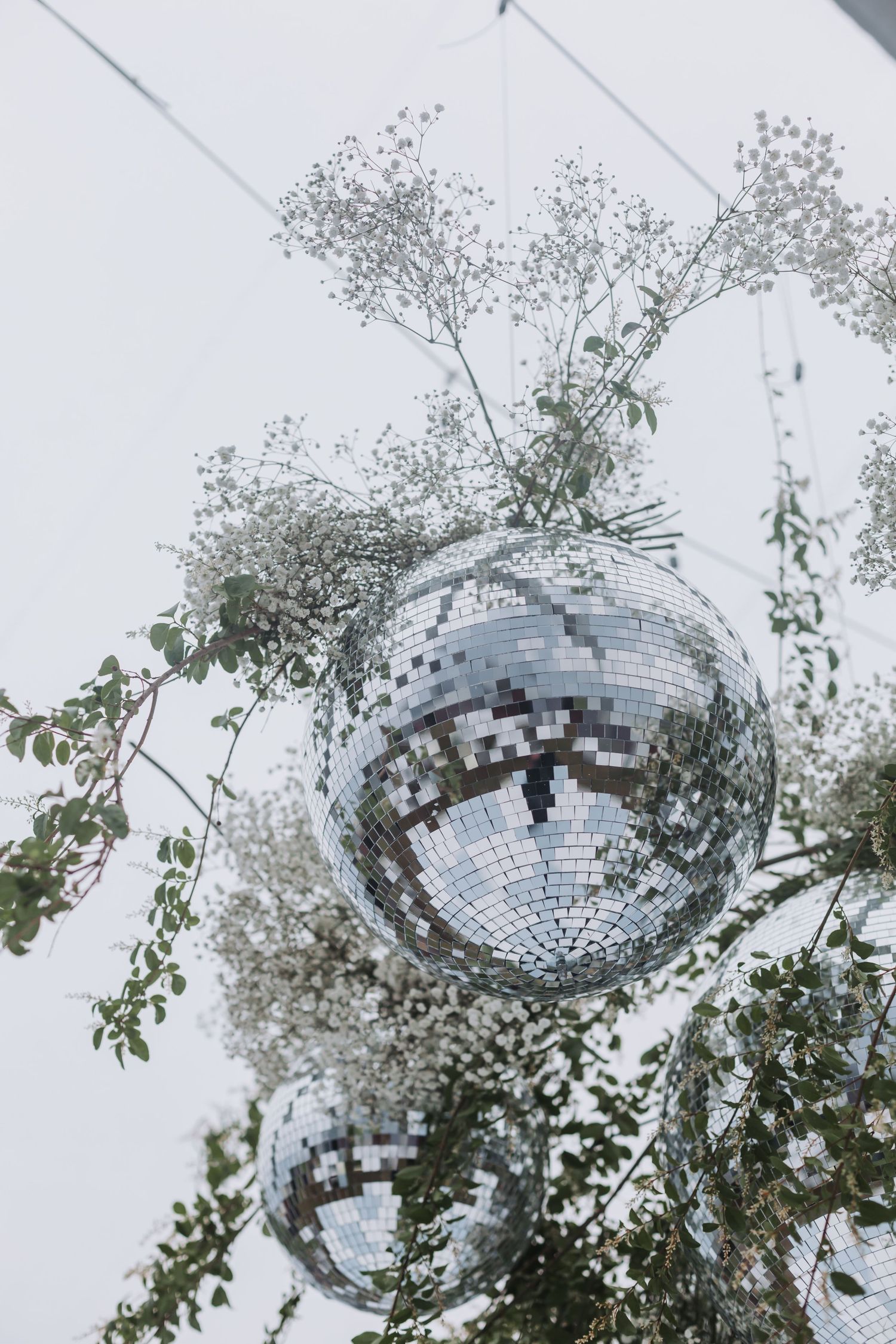 Silver disco ball surrounded by delicate white flowers and green branches against a light background.