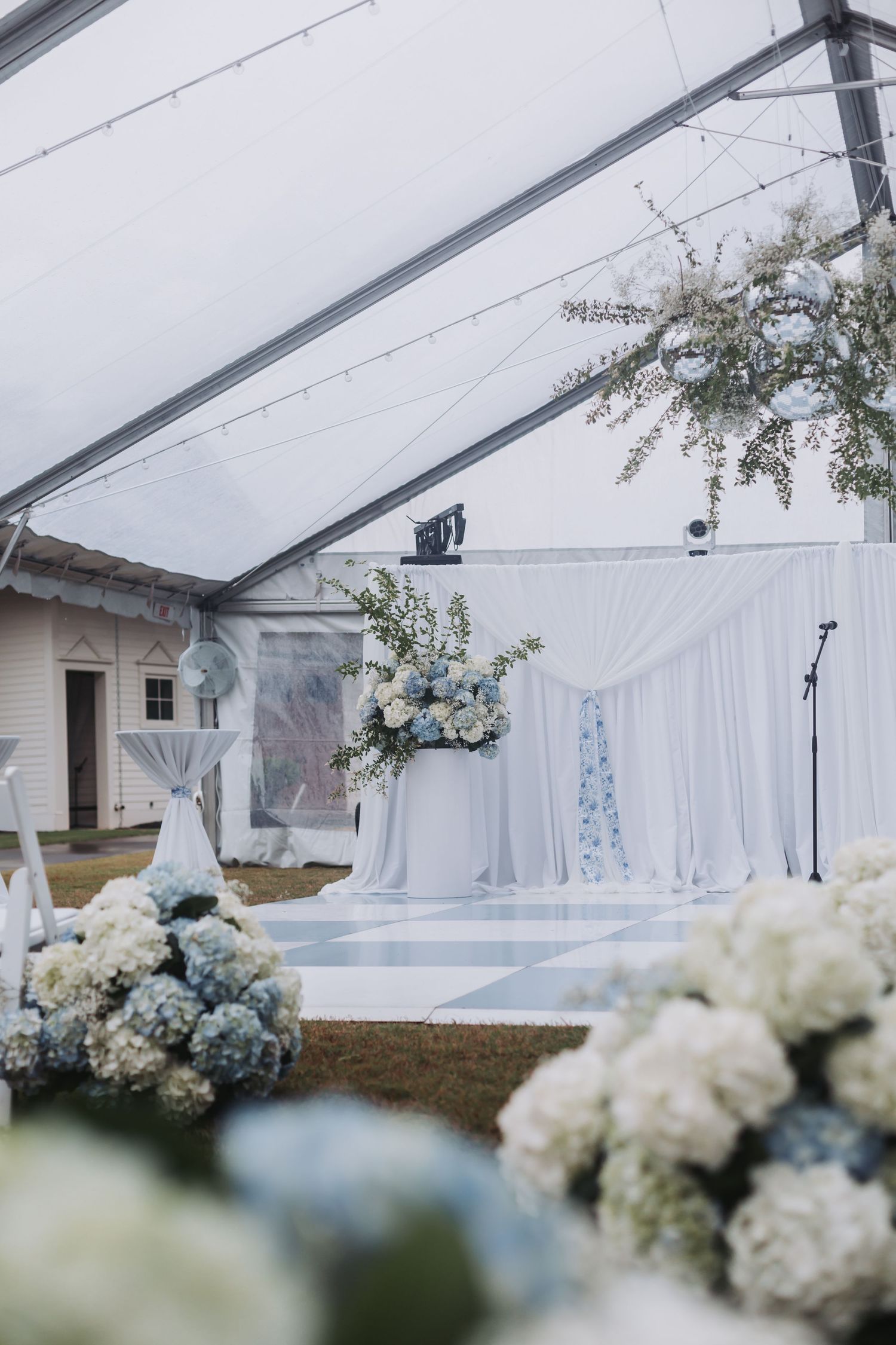 Elegant wedding ceremony setup under a tent with blue and white hydrangeas and floral arrangements.