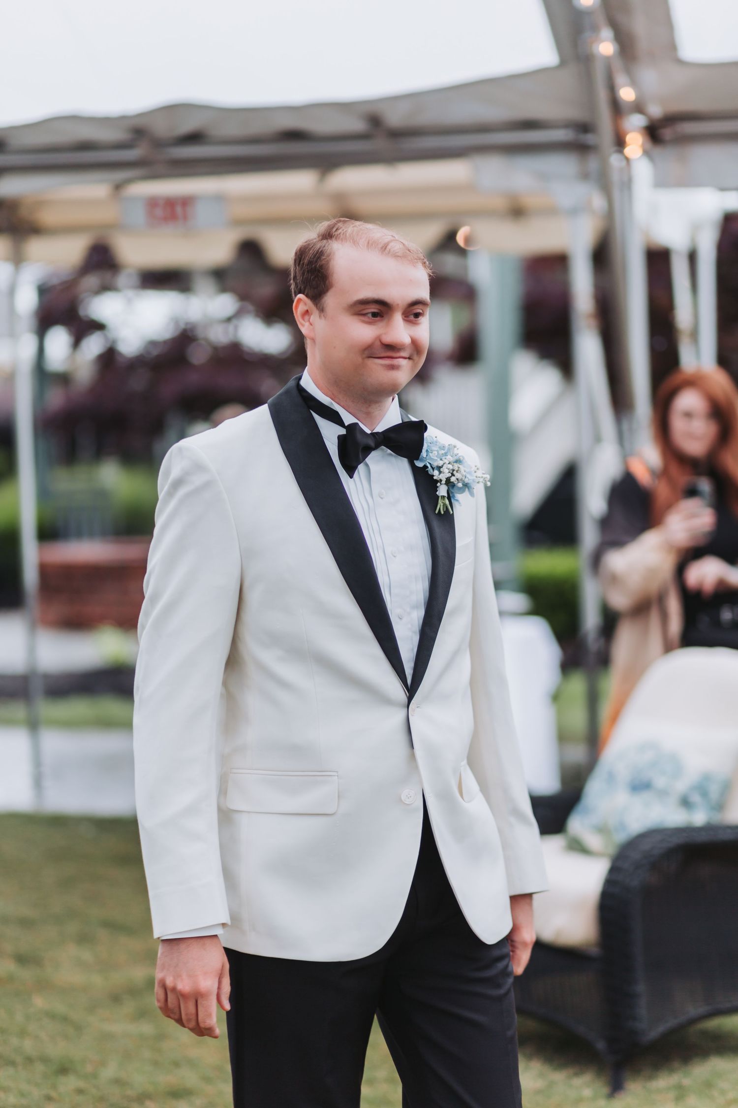 Handsome groom in white tuxedo jacket with black lapels and floral boutonniere at outdoor wedding.