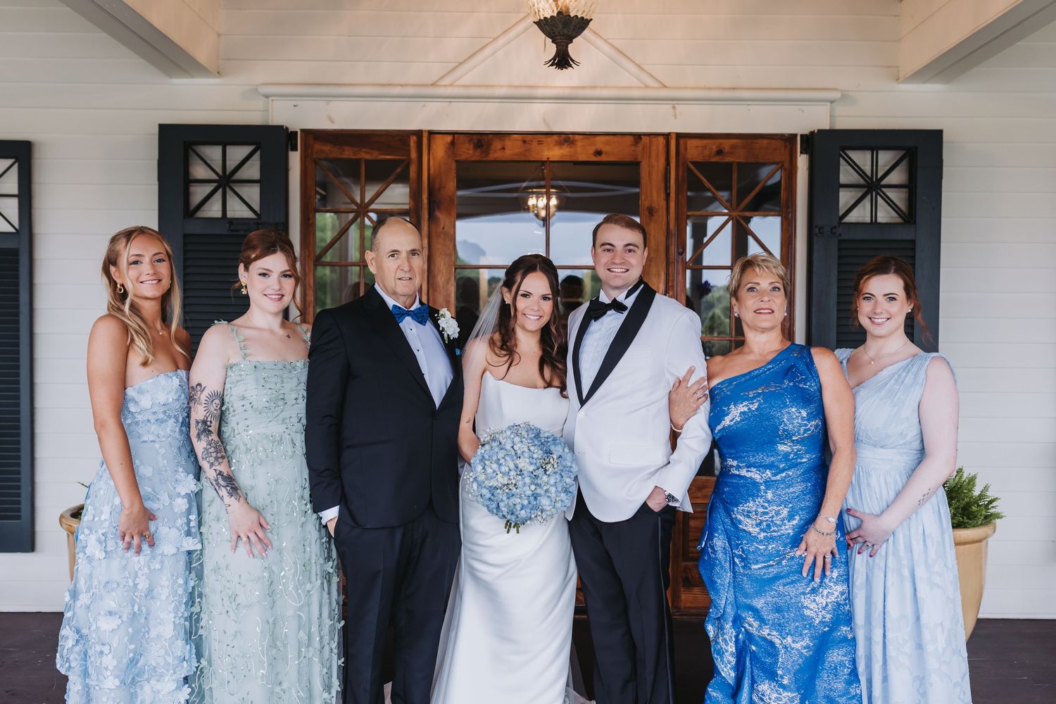 Wedding family portrait of seven adults in formal attire outside venue entrance.