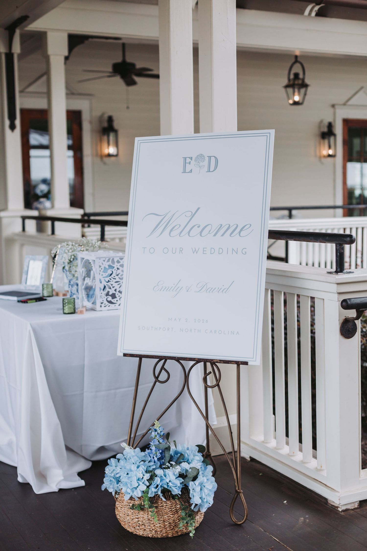 White wedding welcome sign for Emily and Daniel on easel with blue hydrangeas at venue entrance.