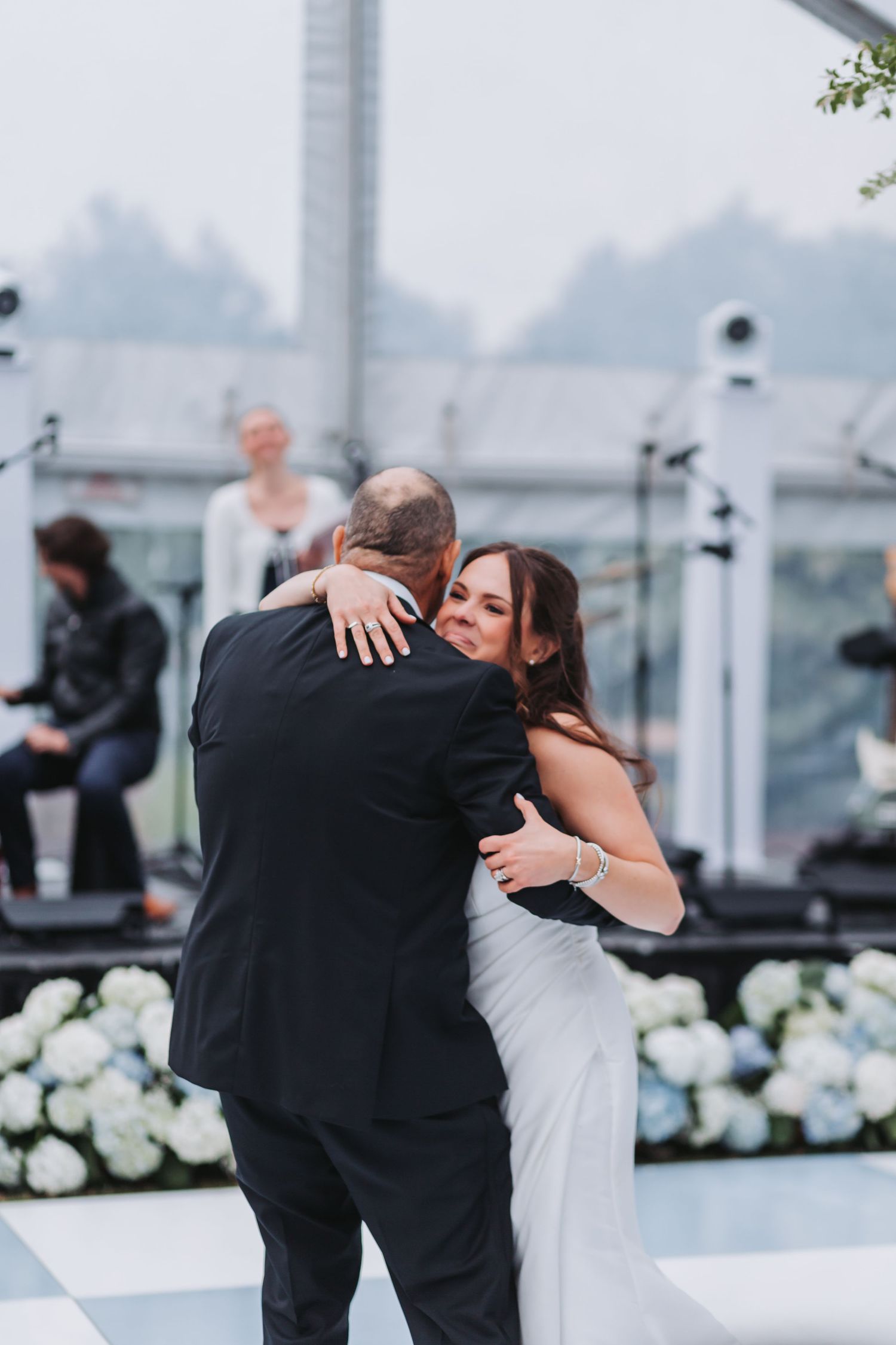 Bride and father share emotional dance at elegant outdoor wedding reception with white hydrangea floral arrangements.