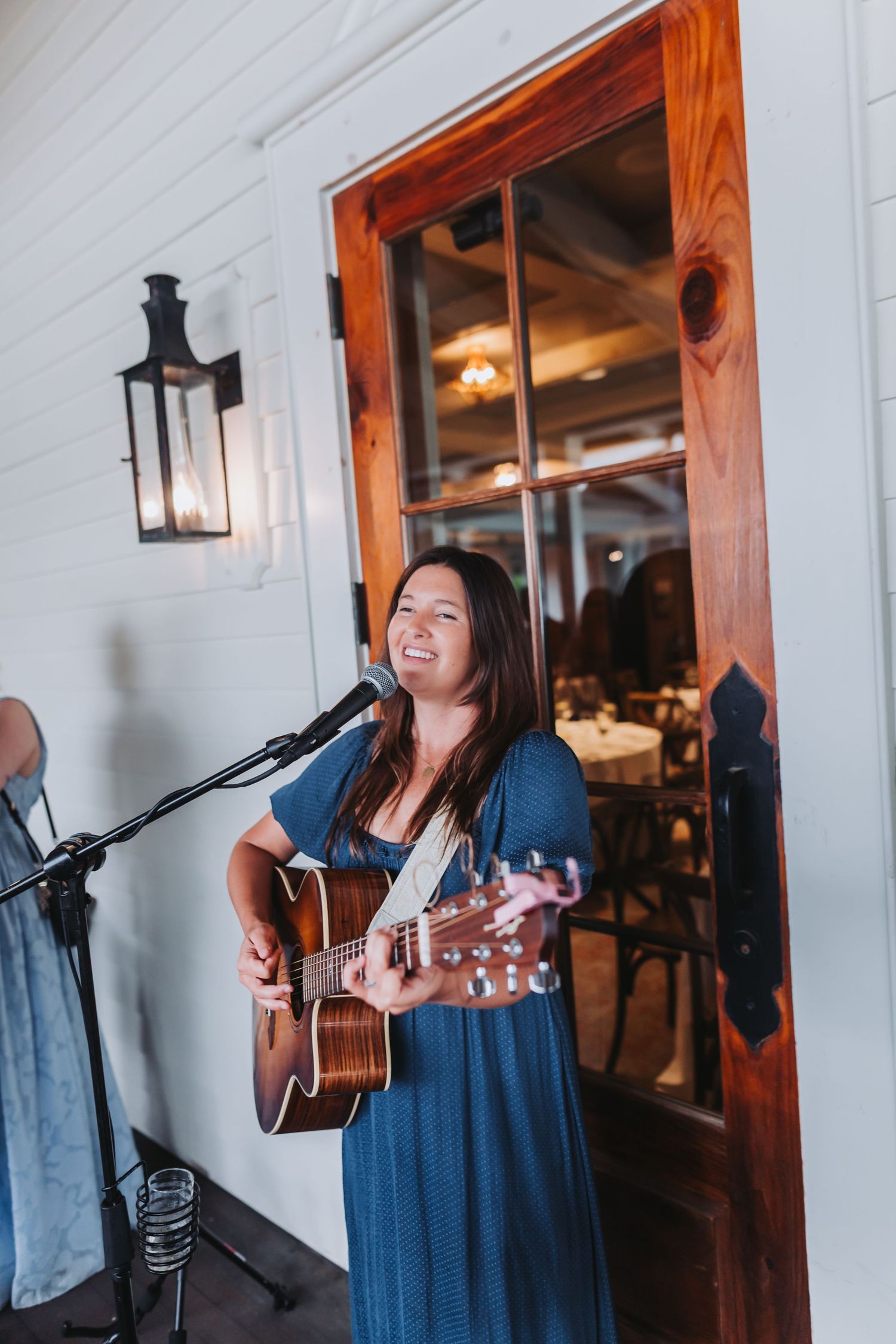 Female musician in blue dress playing acoustic guitar and singing at an outdoor wedding ceremony.