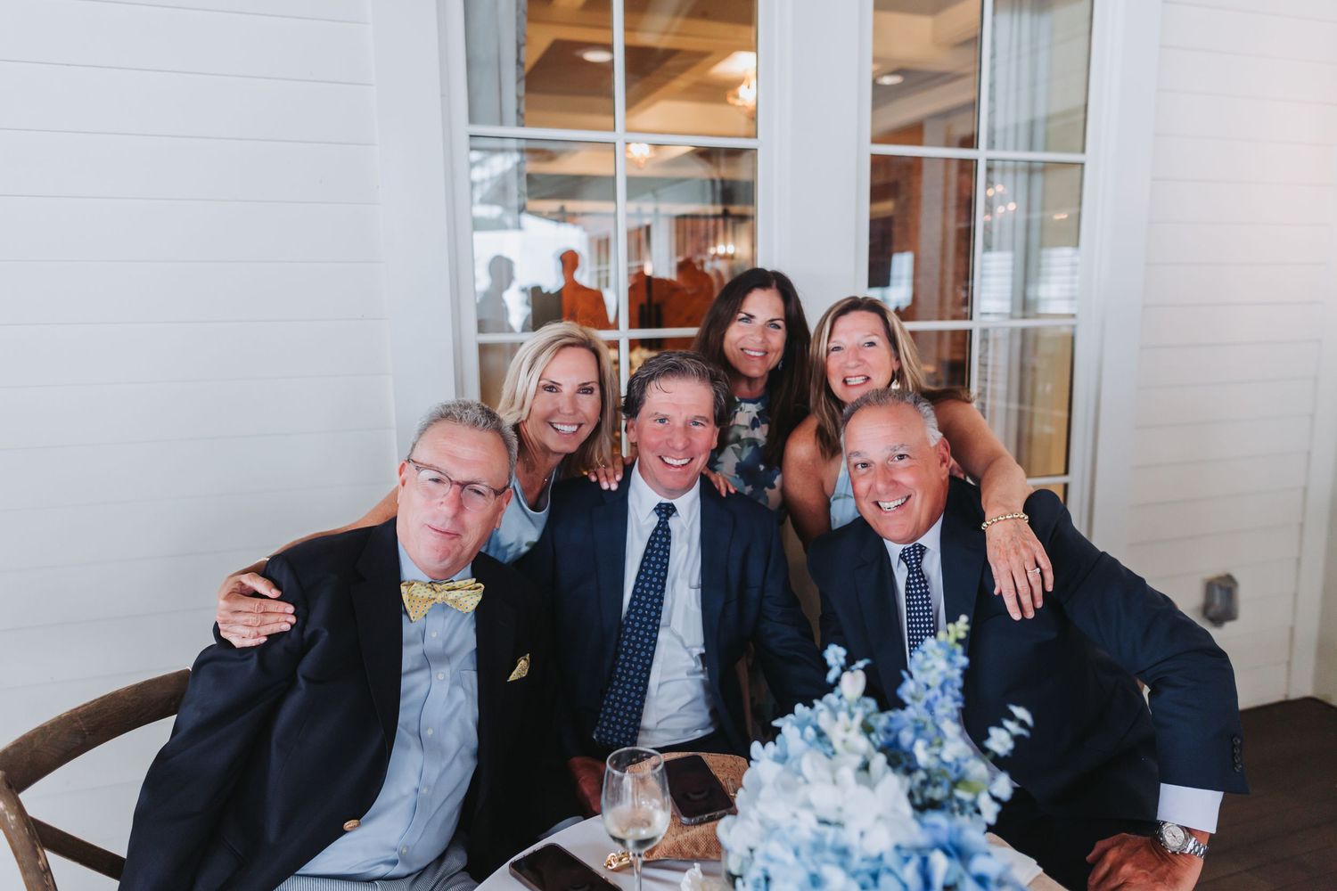 Group of five smiling wedding guests posing together at a table with blue floral decor.