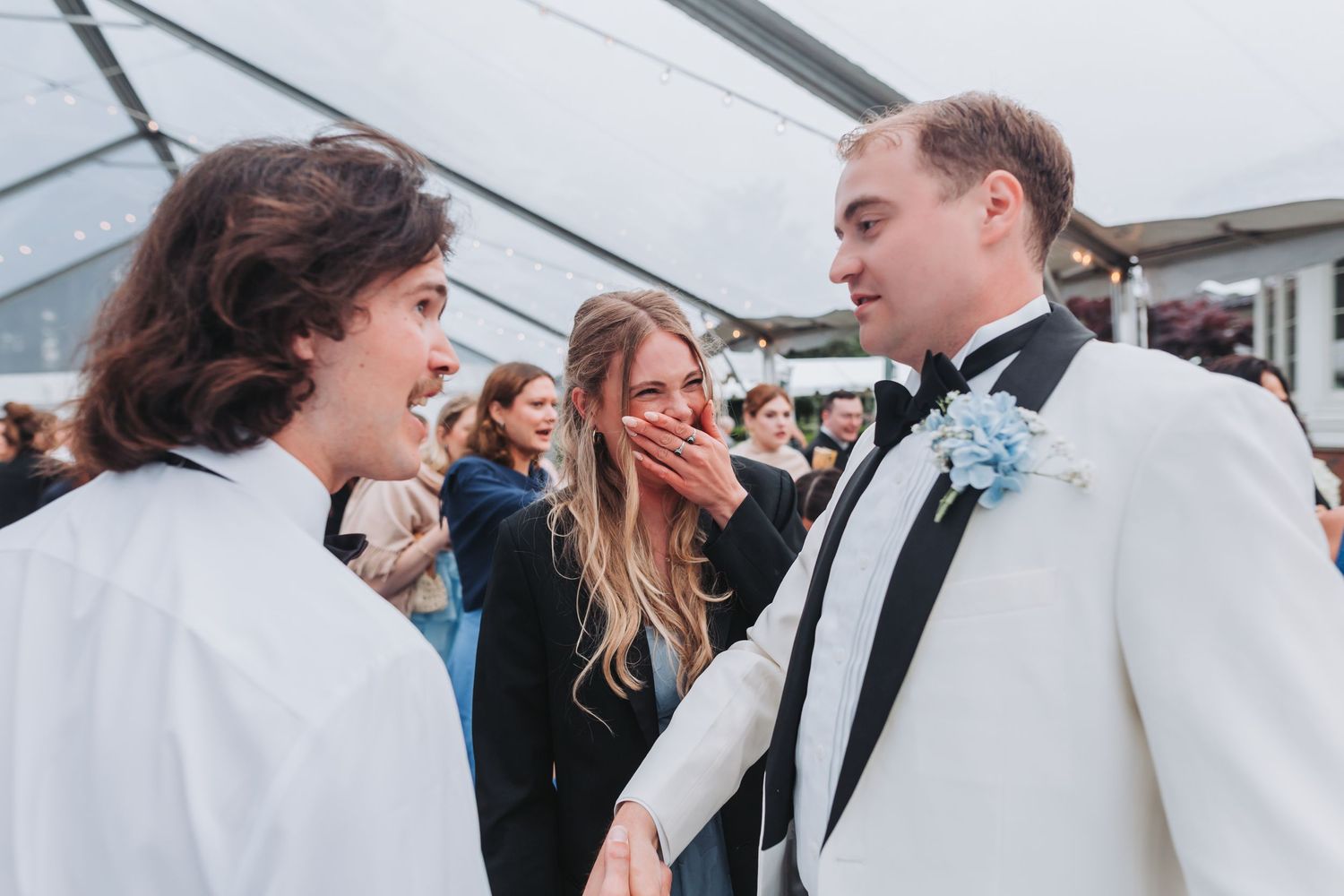 Groom in white tuxedo greeting emotional wedding guests at elegant outdoor reception venue.