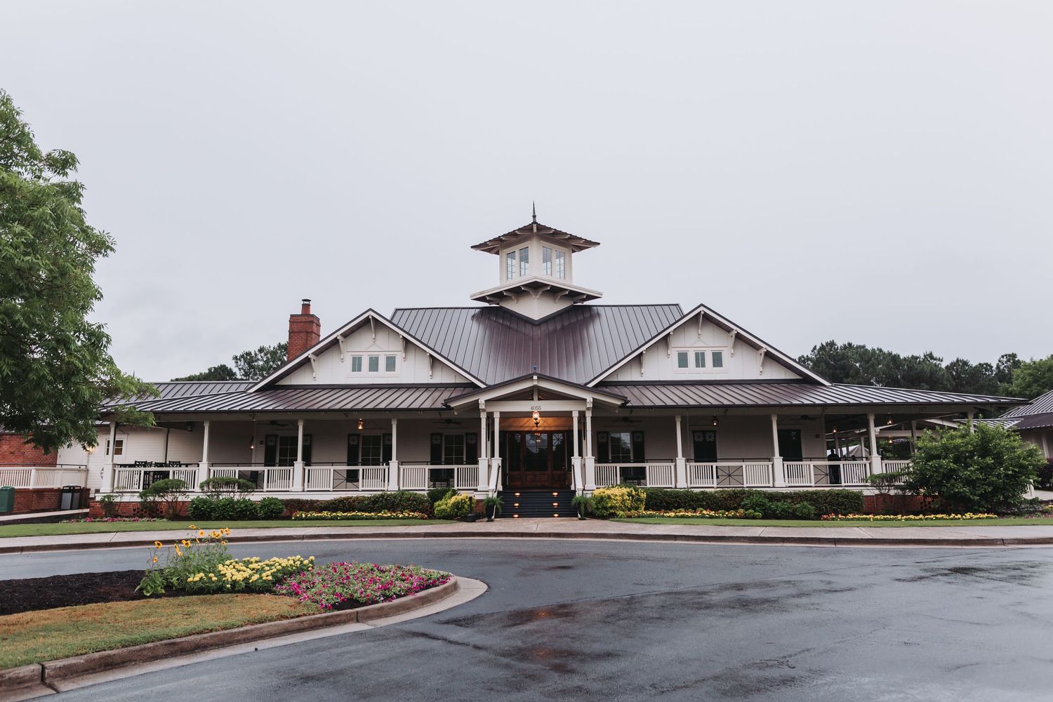 Charming white country club wedding venue with wraparound porch and metal roof on an overcast day.