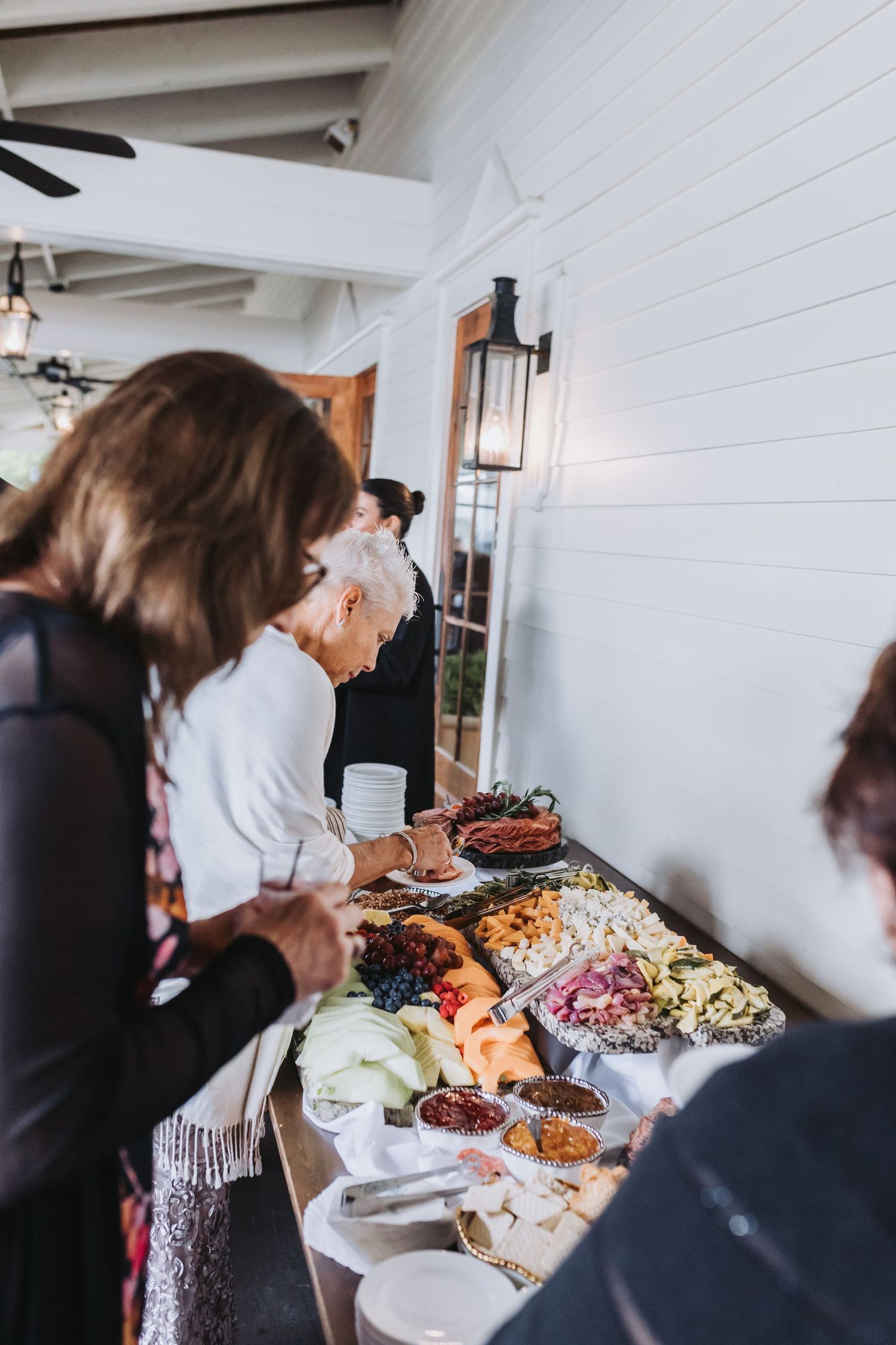 Guests browse an elegant charcuterie and fruit spread at a wedding reception buffet table.