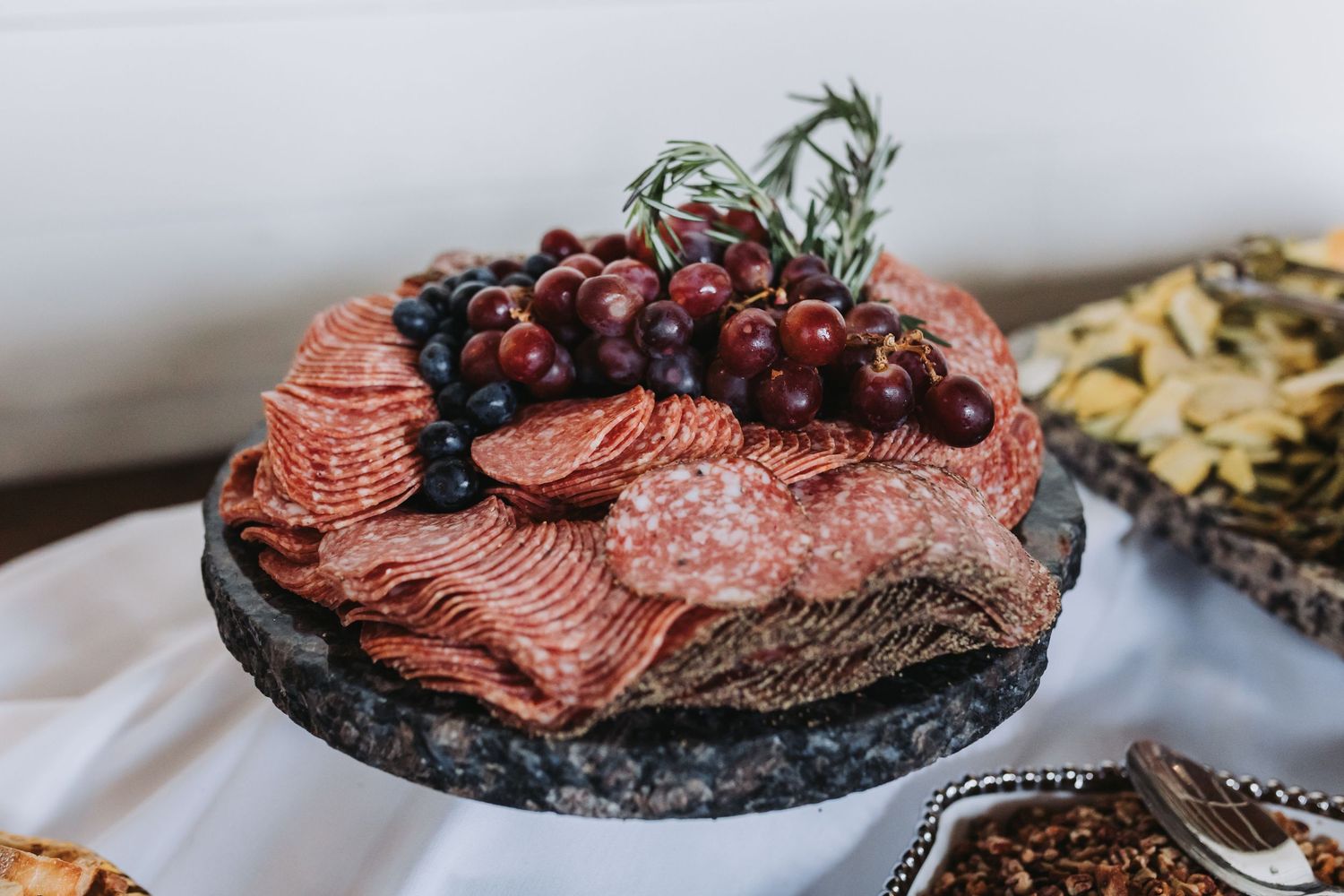 Elegant charcuterie board with sliced salami, red grapes, blueberries, and rosemary garnish on a marble platter.