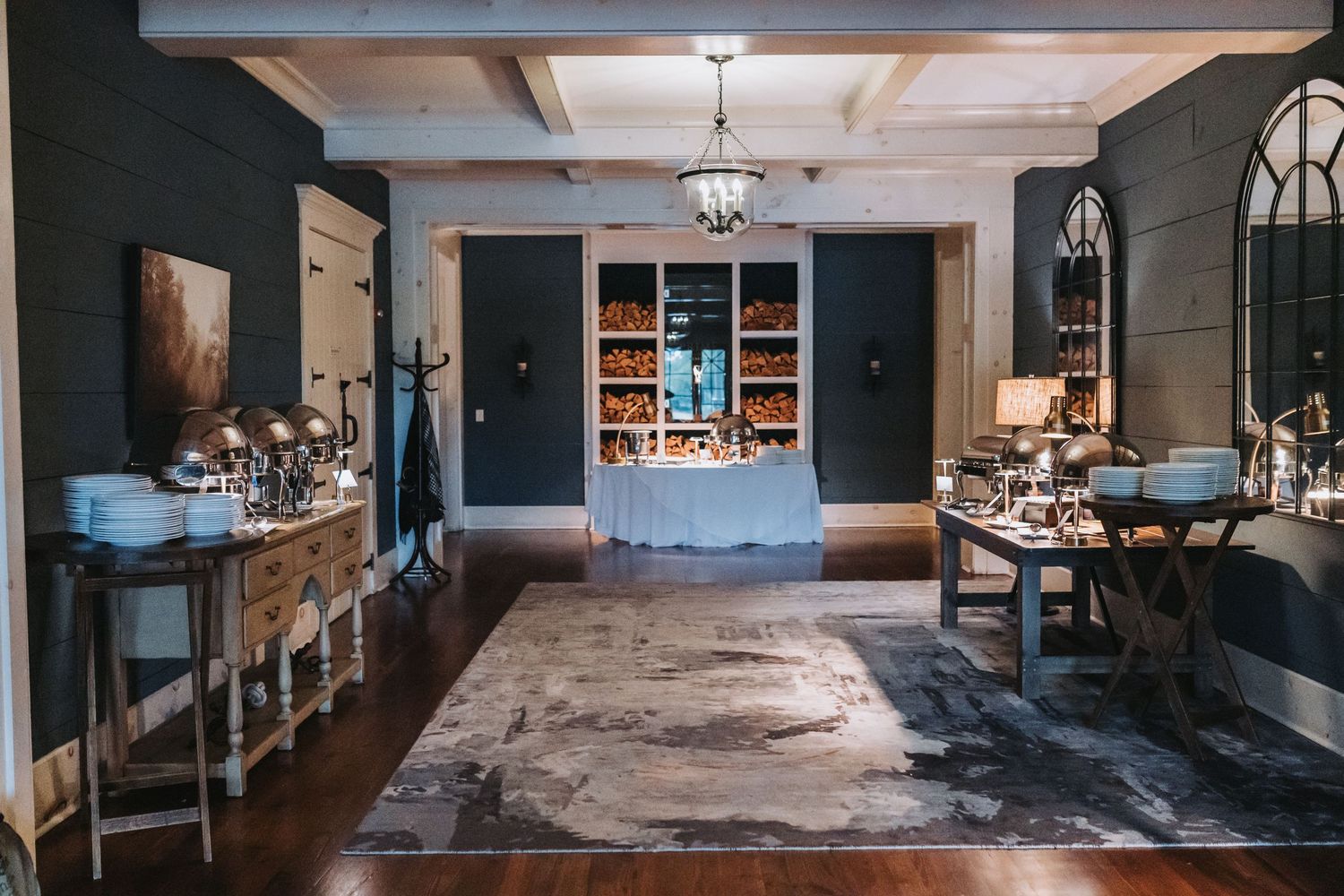 Elegant dark-walled venue interior with chandelier, hardwood floors, and a dessert display table in the background.
