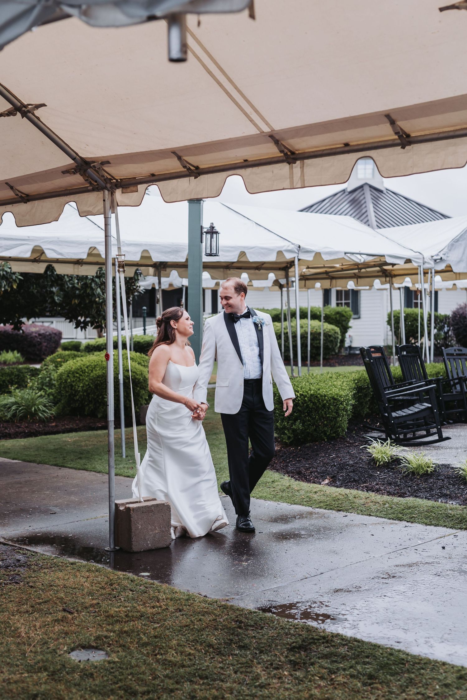 Bride and groom holding hands walking under a tent on a rainy wedding day at an elegant outdoor venue.