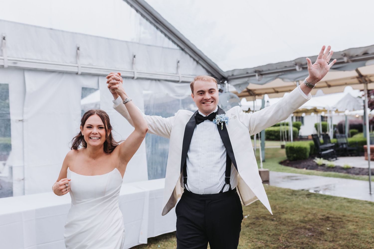 Joyful bride and groom raising hands celebrating their grand entrance at outdoor wedding reception.
