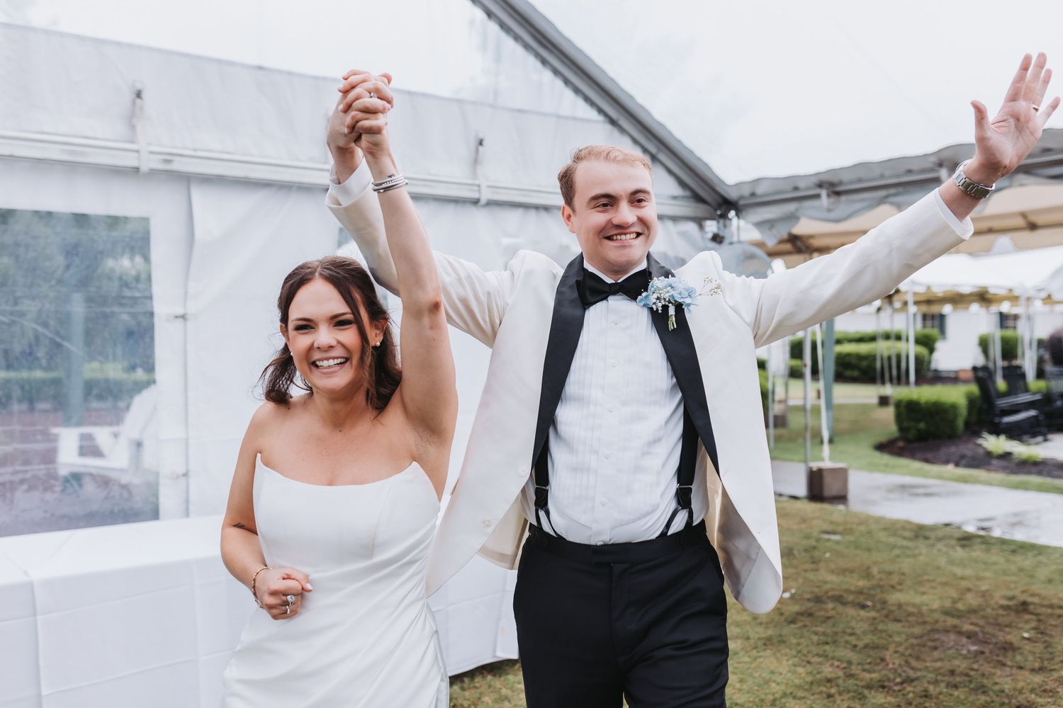 Happy newlyweds smiling and raising hands together during their celebratory wedding reception entrance.