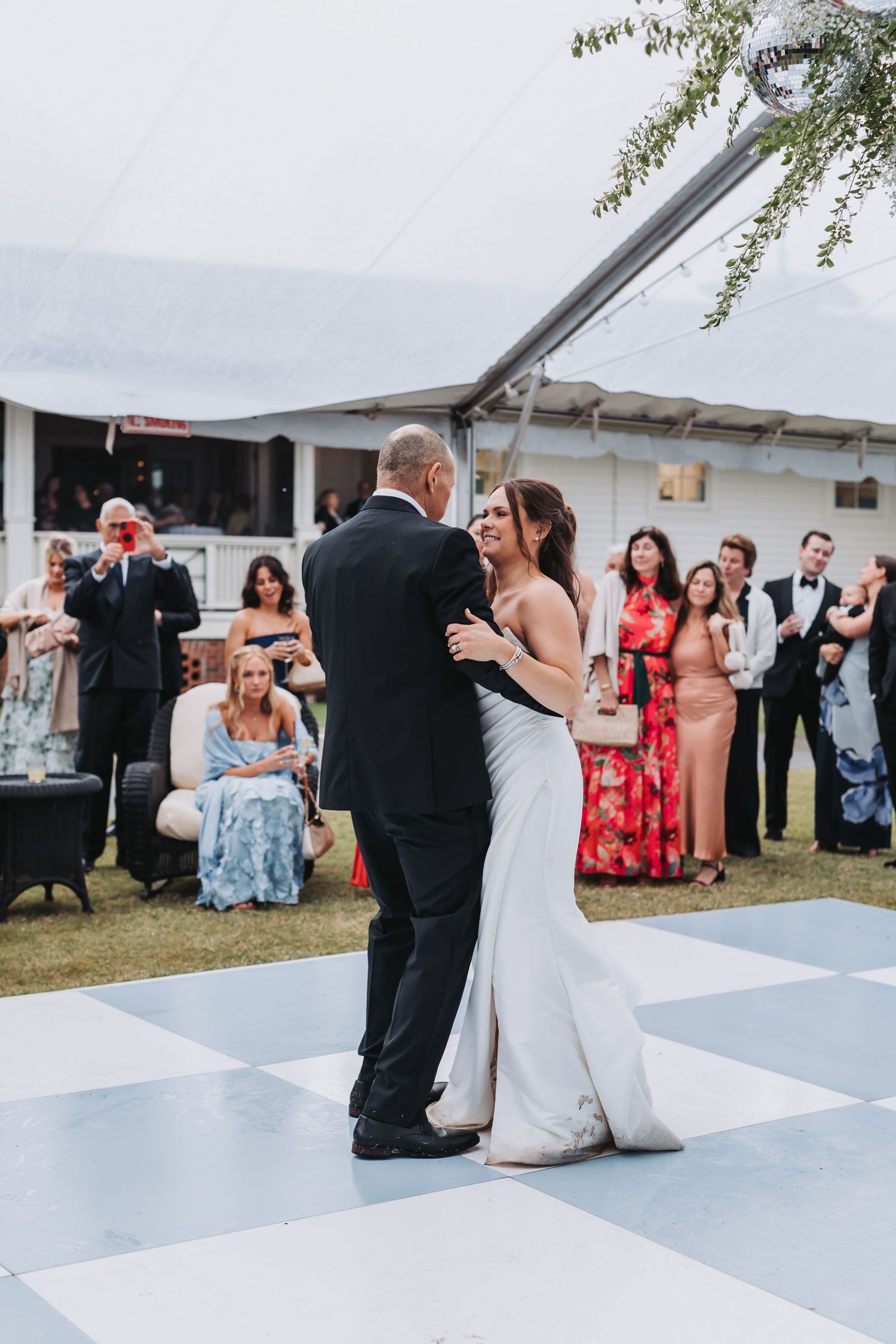 Bride and groom share their first dance on a checkered floor surrounded by wedding guests.