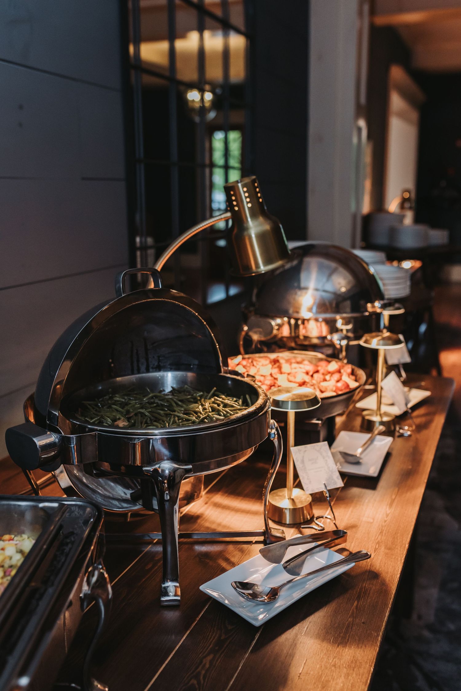 Elegant wedding buffet with chafing dishes filled with green beans and shrimp on a wooden table.
