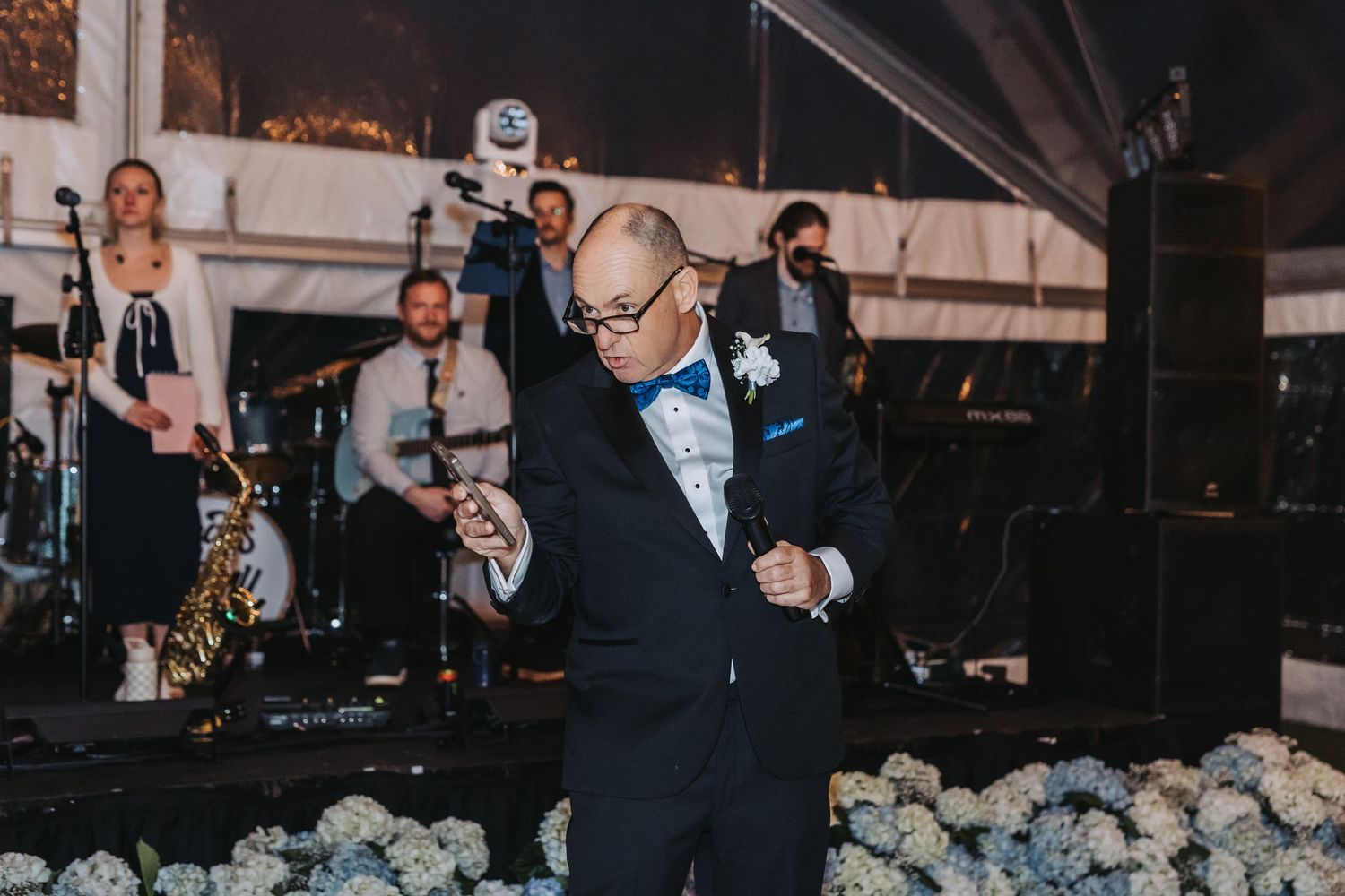 Father of the bride dancing joyfully in black tuxedo at elegant outdoor tented wedding reception.