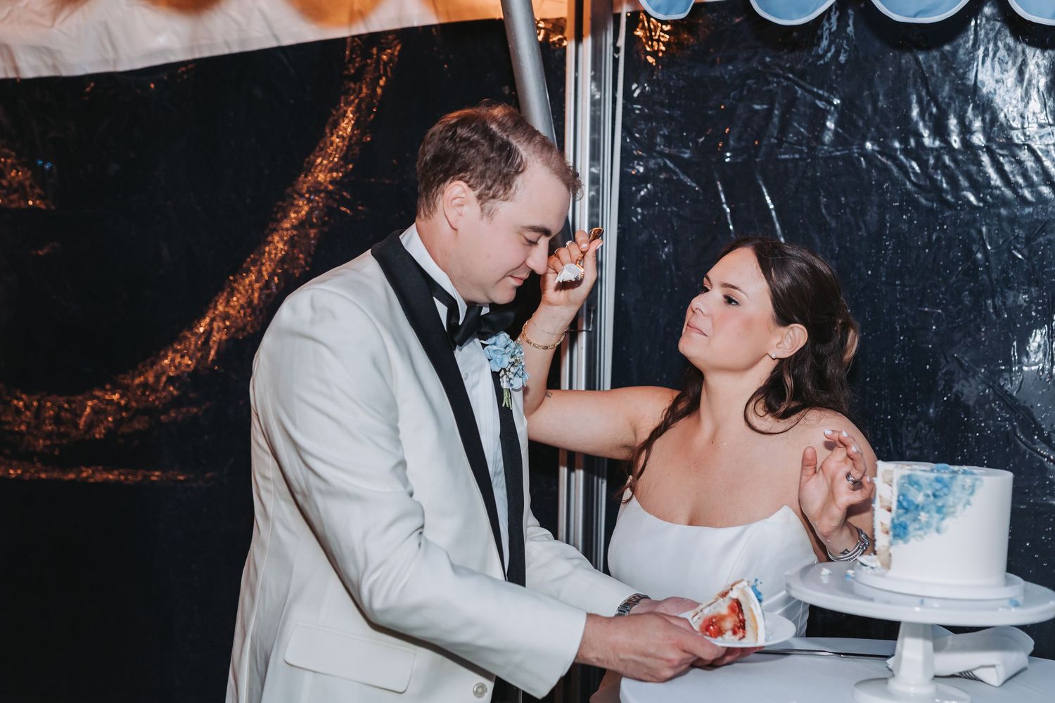 Bride smashing wedding cake into grooms face during fun cake cutting ceremony at reception.