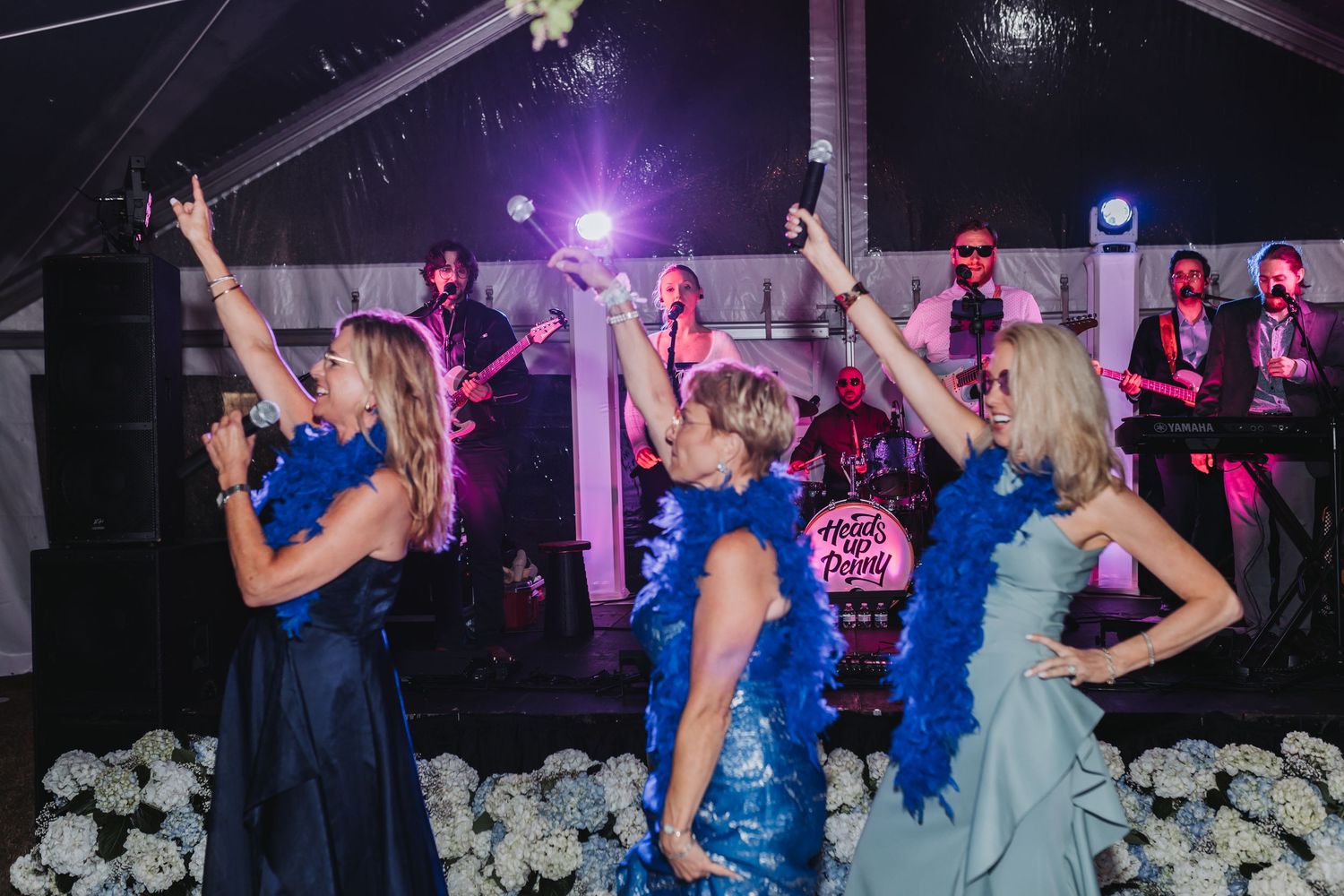 Bridesmaids in blue dresses dancing with raised arms in front of a live band at a wedding reception.