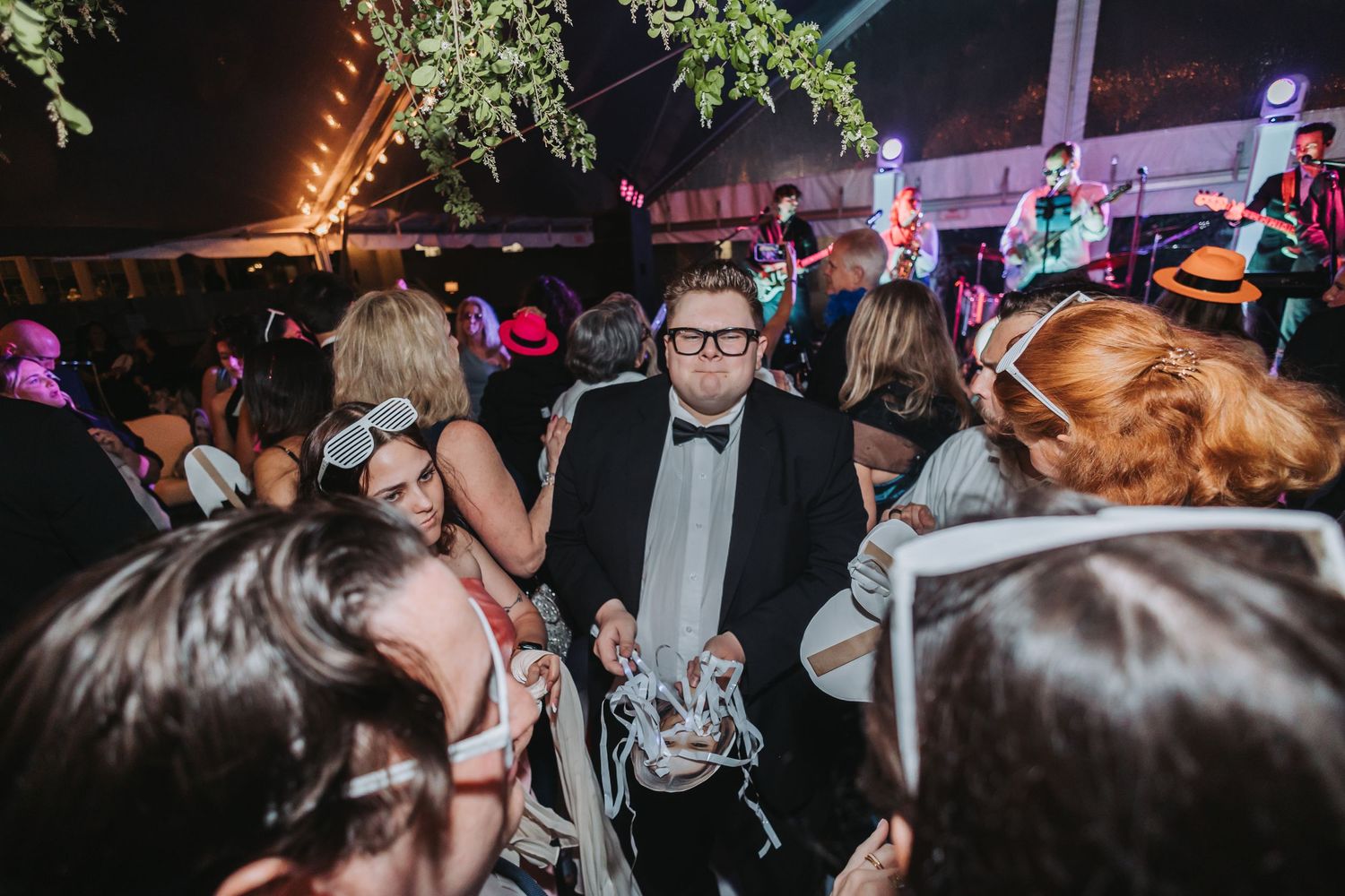 Guests dancing and celebrating at an outdoor evening wedding reception under a tent with live band.