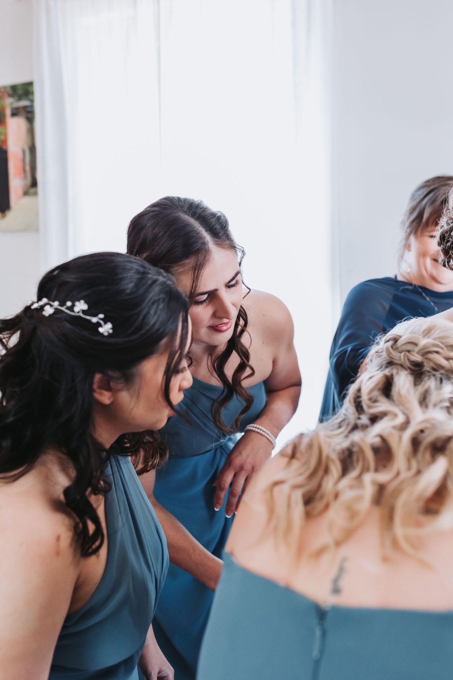 Bridesmaids in blue dresses gather closely together, smiling and sharing a joyful moment during wedding preparations.