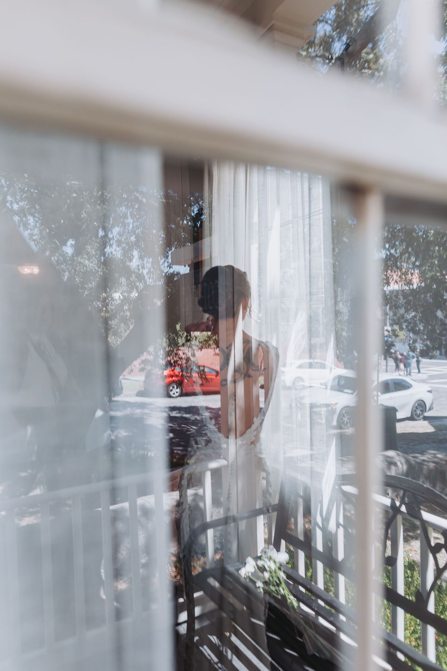 Bride in wedding dress seen through window reflection on her wedding day.
