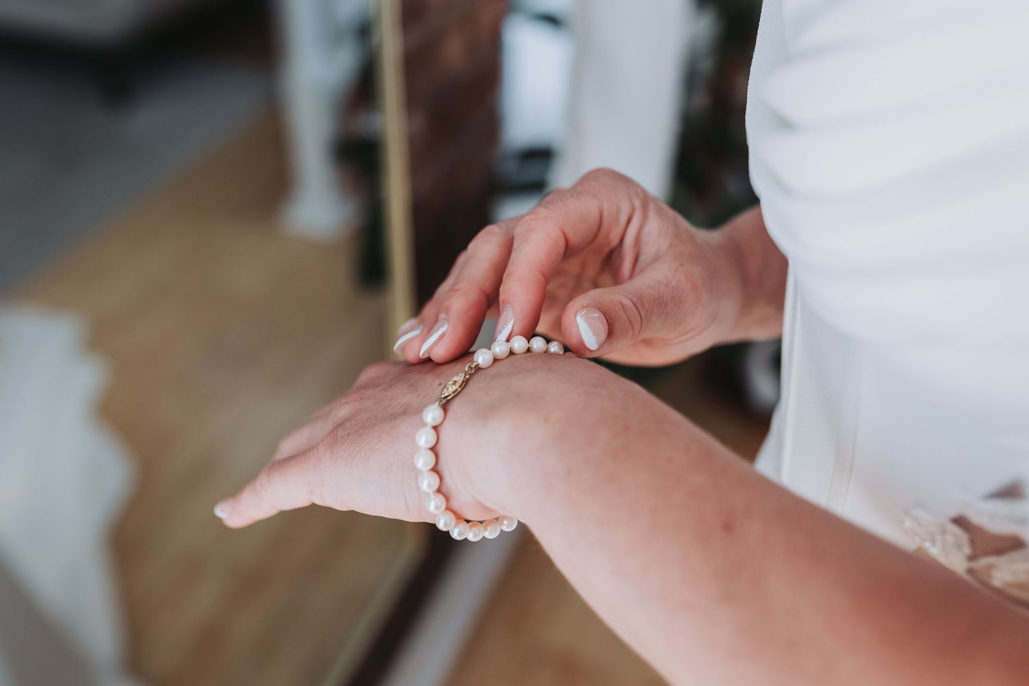 Close-up of bride placing pearl and rose gold bracelet on her wrist.
