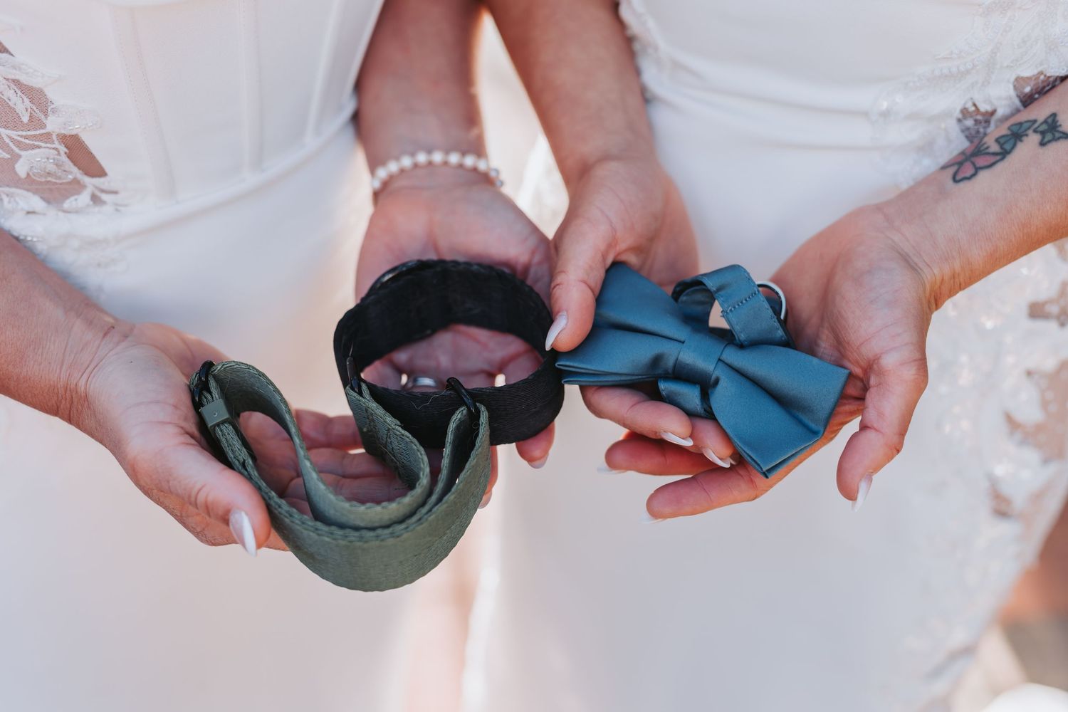 Two brides holding blue bow tie and green tie at wedding ceremony.
