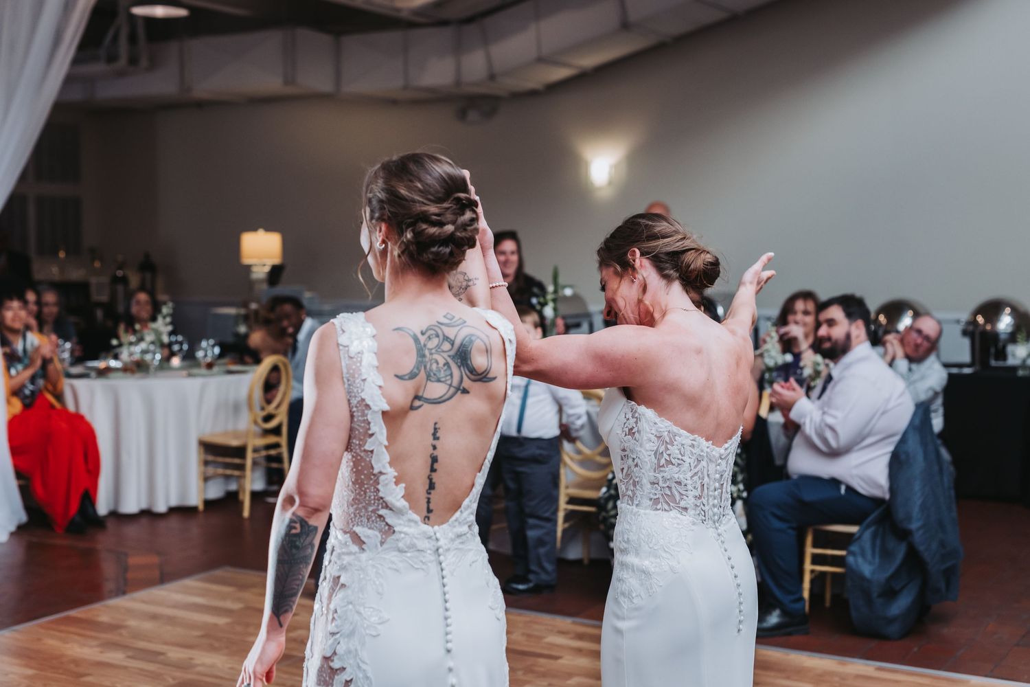 Two brides in white lace gowns sharing first dance at wedding reception.