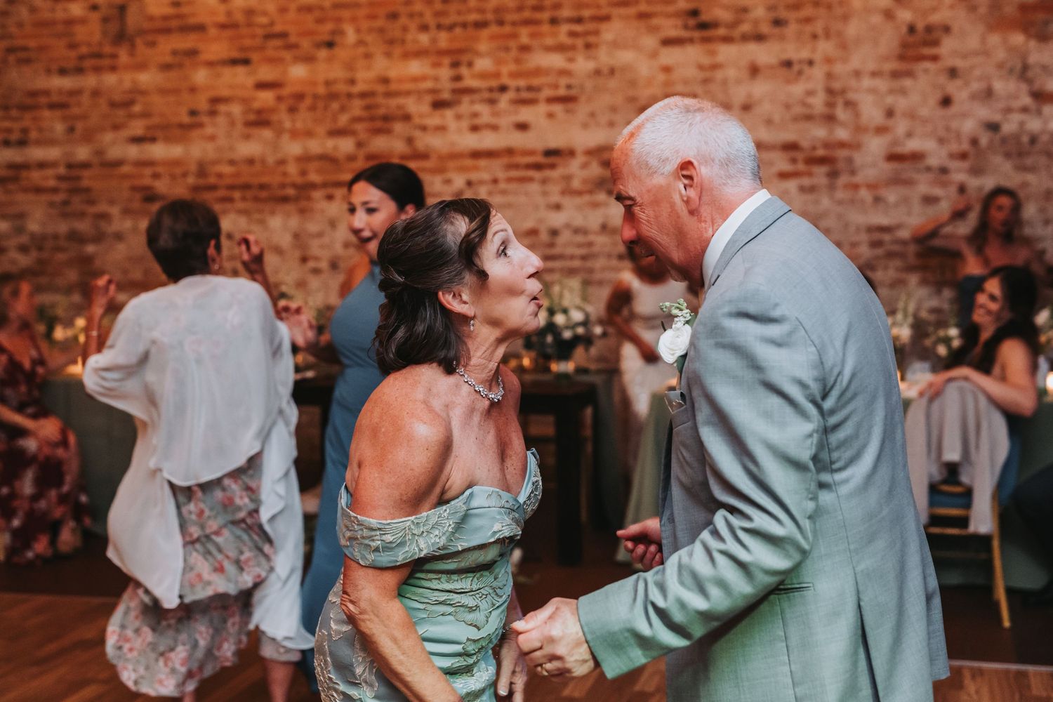 Couple dancing joyfully at a wedding reception in a rustic venue with exposed brick walls.