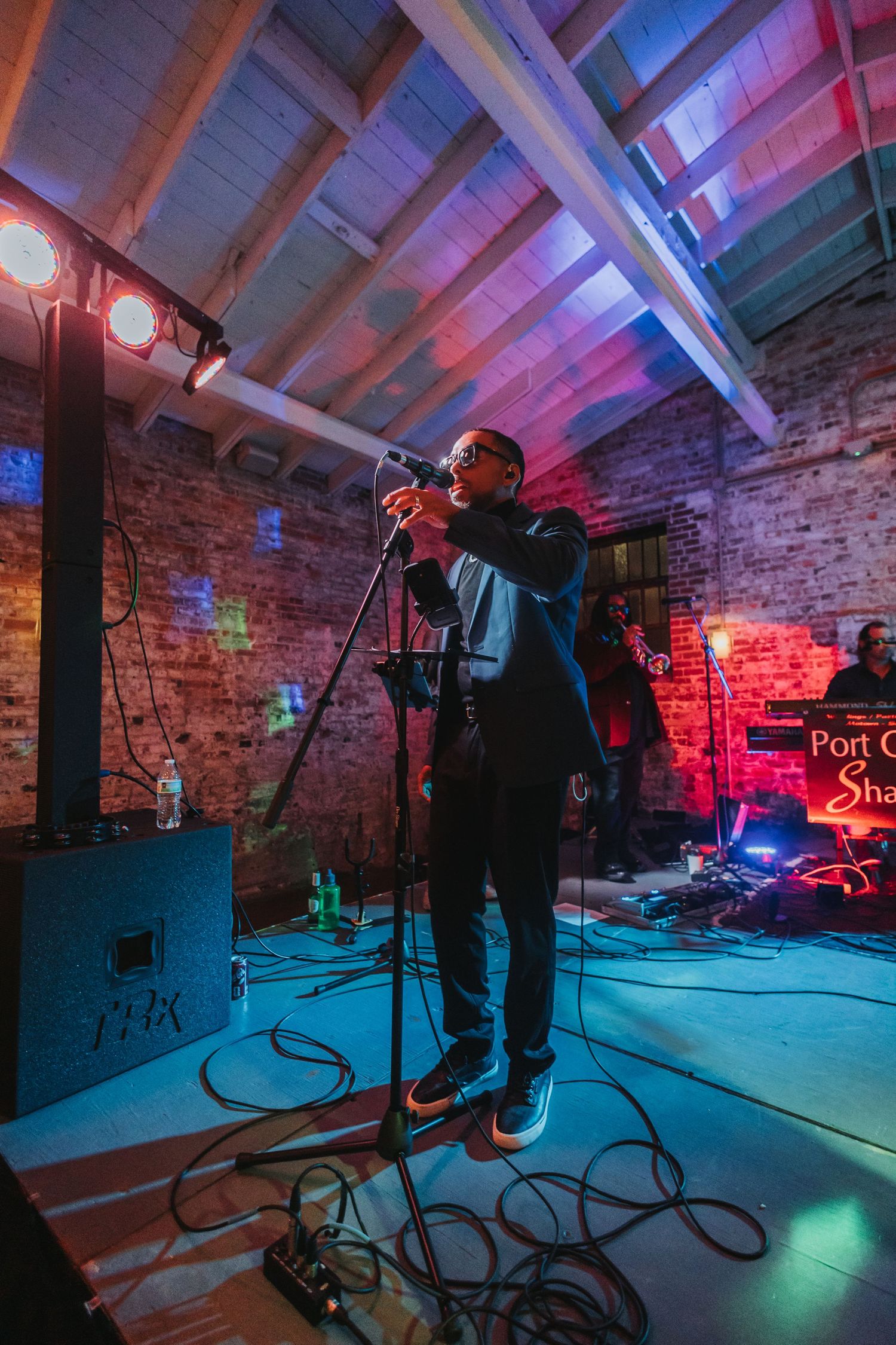 Live performer singing on stage with colorful lights at indoor brick wall venue during wedding reception.