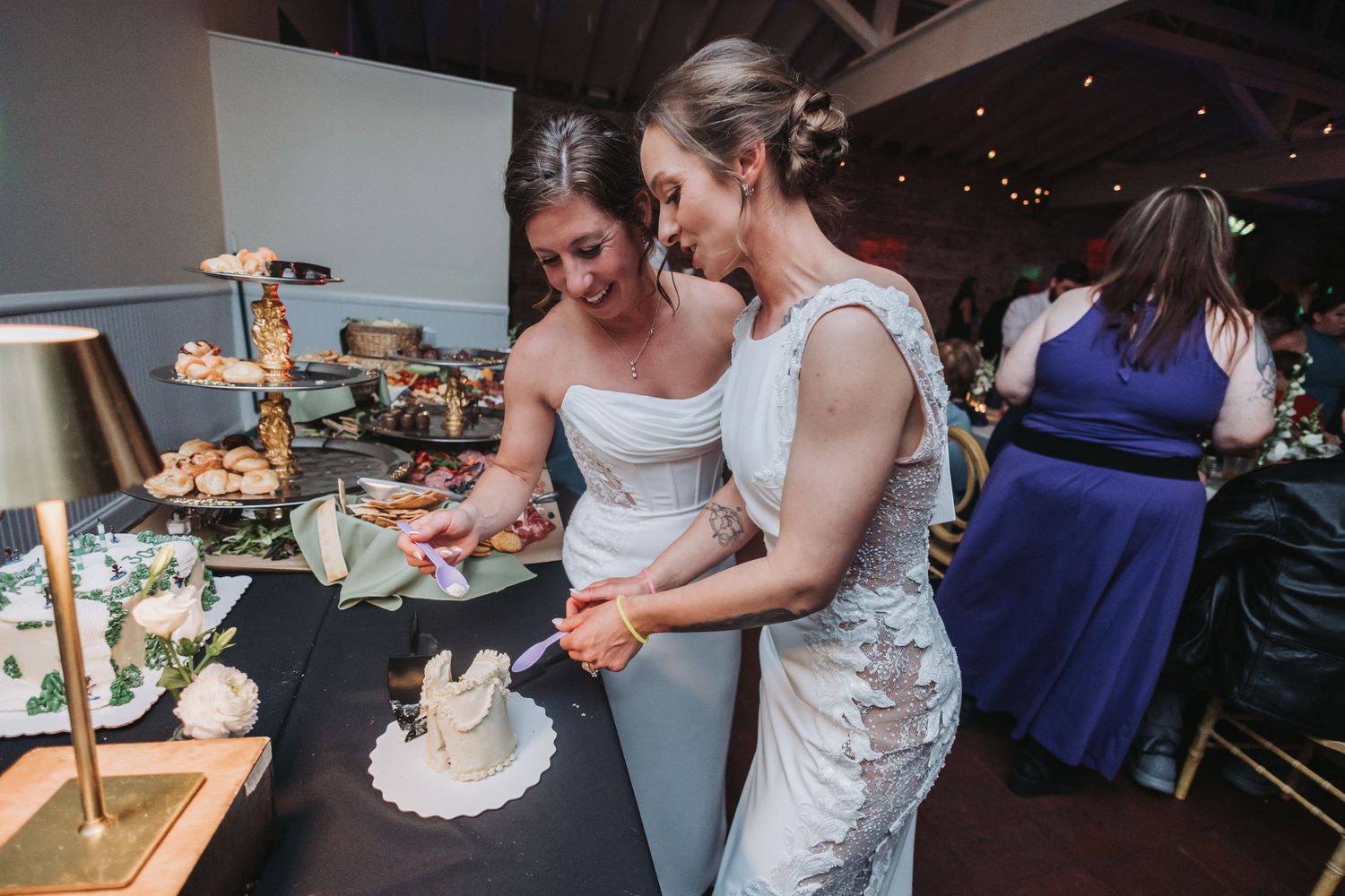 Two brides in white gowns cutting their wedding cake together at a elegant reception venue.