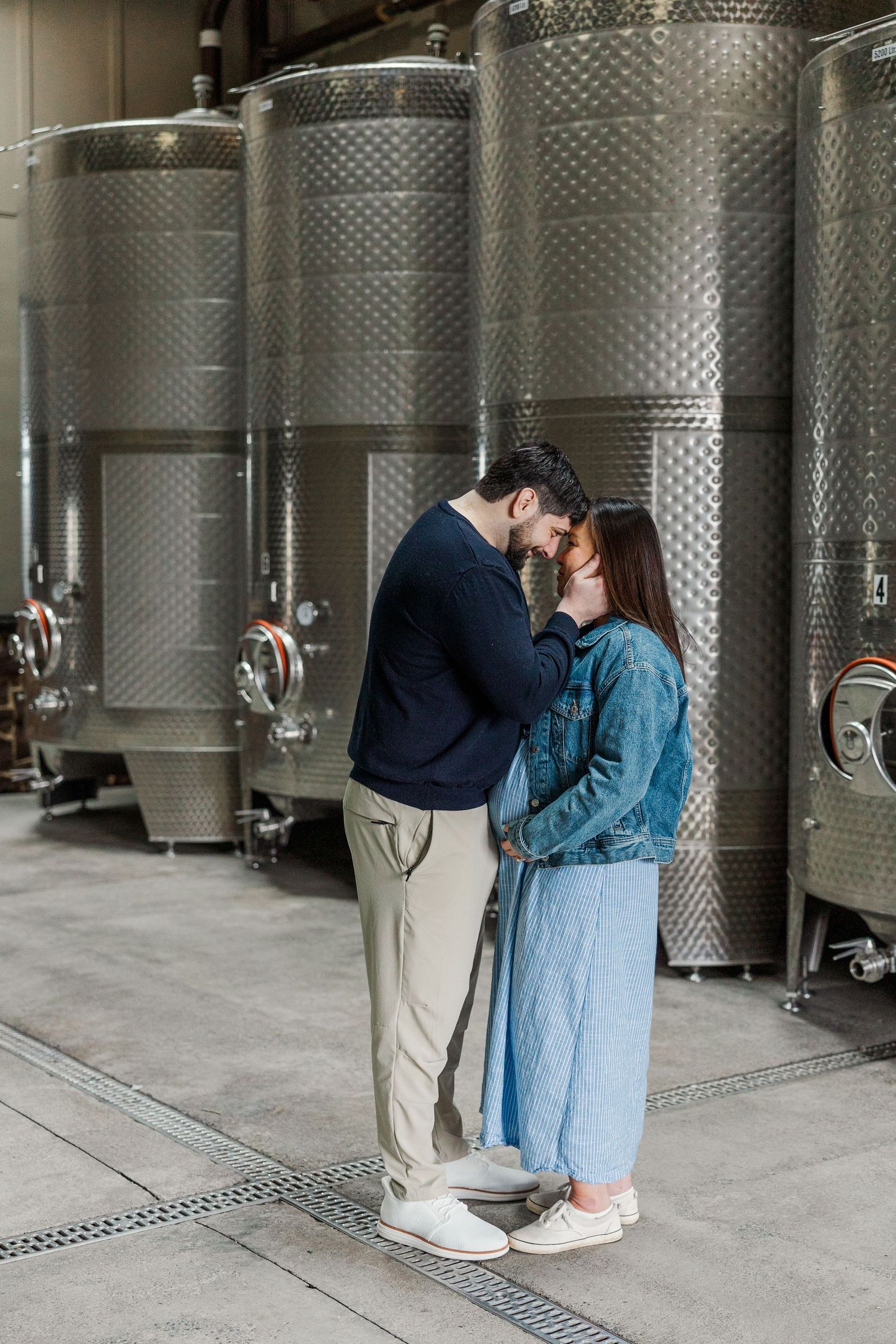 Romantic couple embracing in a modern winery surrounded by stainless steel fermentation tanks.