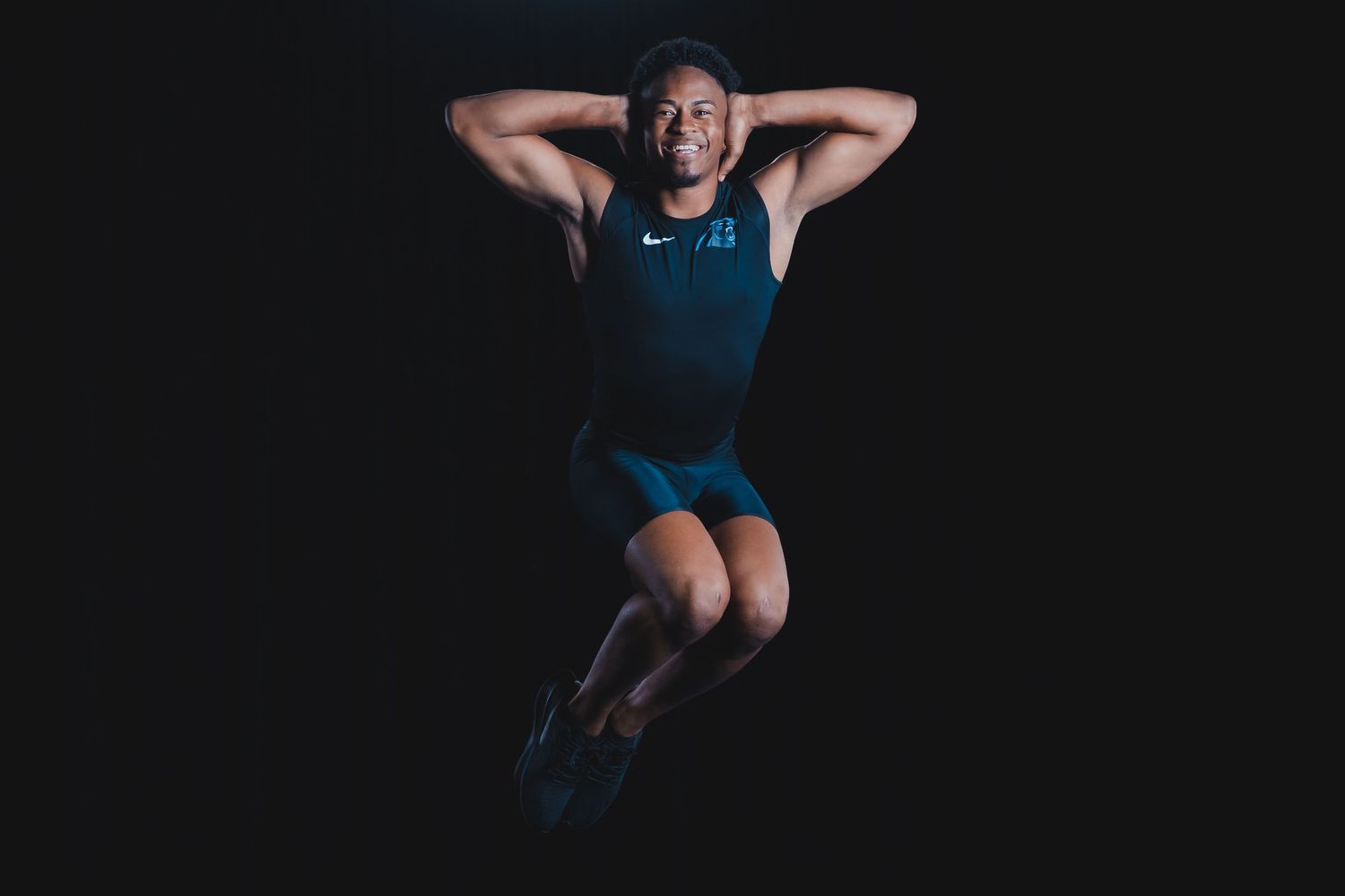 Athletic man in Nike sportswear jumping against black background in dynamic pose.
