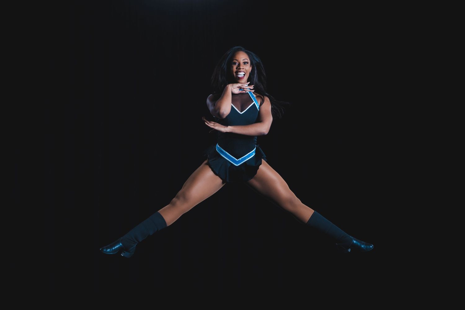 Cheerleader in black and blue LED uniform performs splits against dark background.