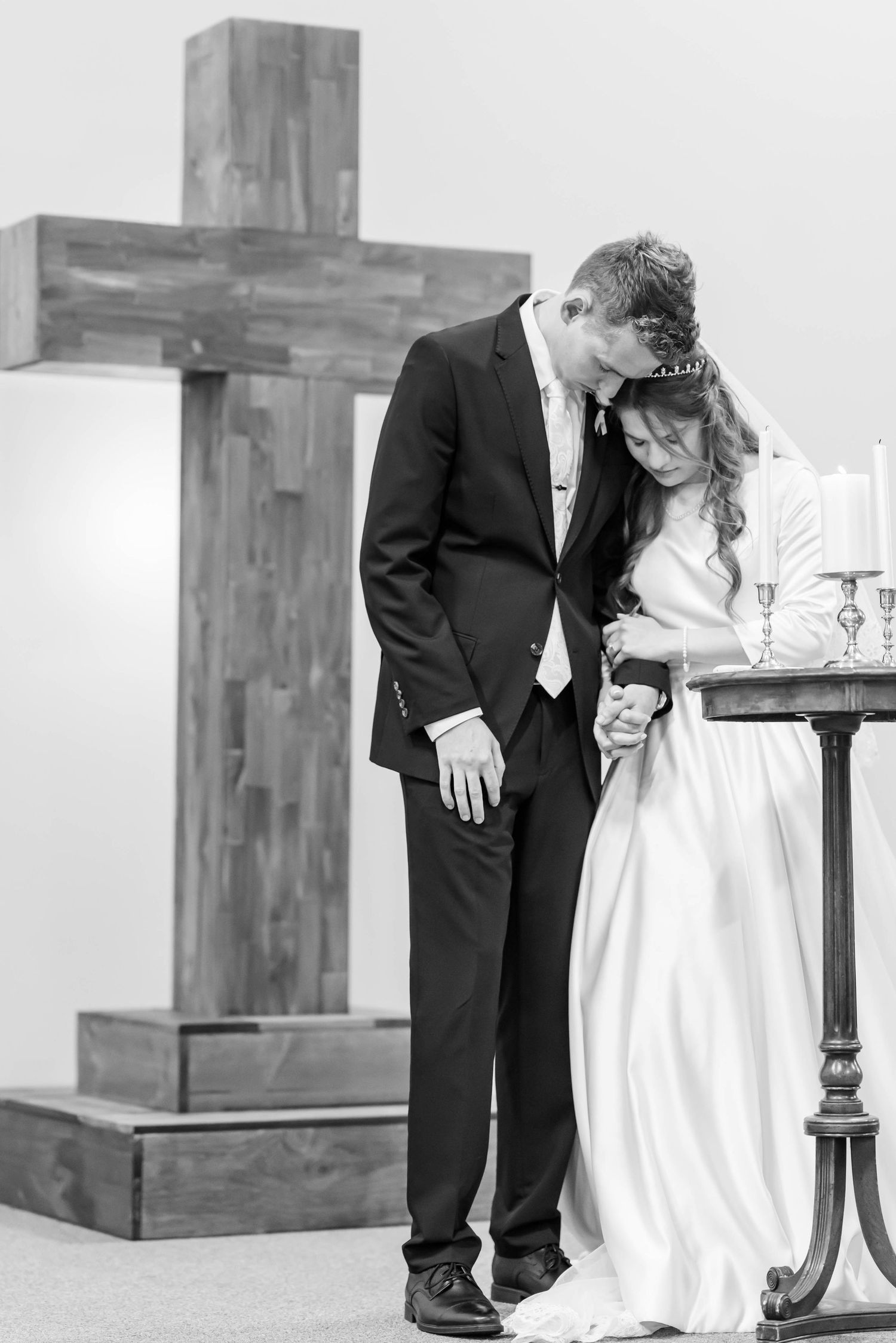 Black and white photo of a bride and groom praying together at the altar with a wooden cross behind them.